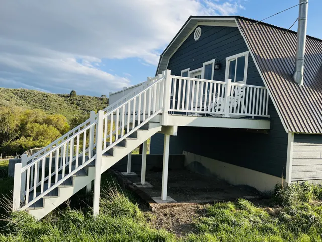 Gambrel roofline property featuring dark blue siding, a white-railed elevated deck, and an exterior staircase with white railings