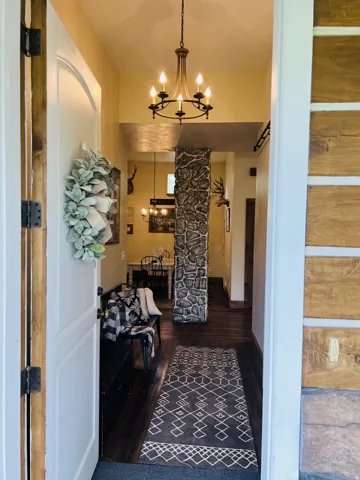 Entryway featuring a stone-clad architectural column, wood-finish flooring, and a chandelier with a dark bronze finish