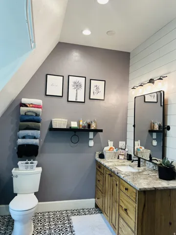 Bathroom featuring patterned floor tiles, a rustic wood-finish vanity with a stone countertop, a rectangular undermount sink, and a black-framed mirror with globe lighting