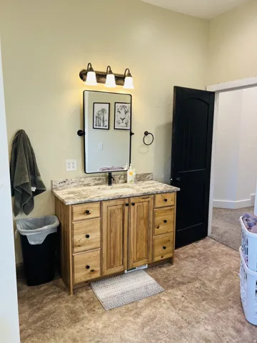 Bathroom vanity featuring a wood-finish cabinet, stone-look countertop, and single basin sink with a matte black faucet