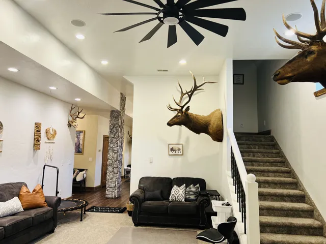 Spacious interior featuring a contemporary ceiling fan, recessed lighting, a stone-clad pillar, and a carpeted staircase with a white and black spindle railing
