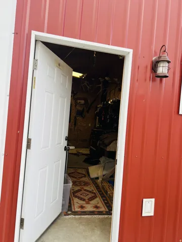 Red corrugated metal siding exterior featuring a white paneled door with black hardware, white trim, and an exterior wall lantern
