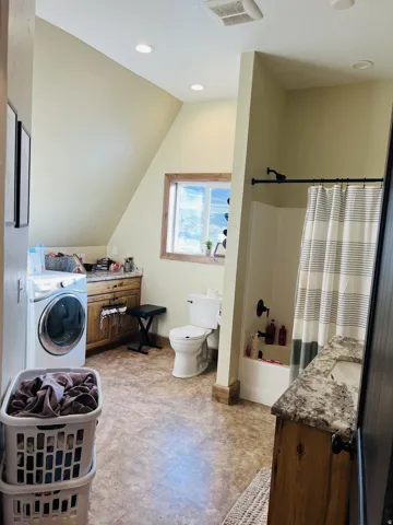 Bathroom featuring wood-finish flooring, a white bathtub with a dark shower fixture, a vanity with a stone-finish countertop and undermount sink, and recessed lighting