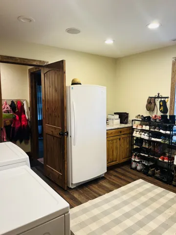 Laundry area featuring wood-finish flooring, recessed lighting, a built-in wood cabinet with a light-toned countertop, and a solid wood door with dark hardware