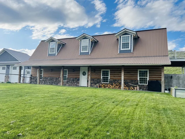 Barn-style home featuring a metal roof, dormer windows, stone facade, log siding, and a covered front porch