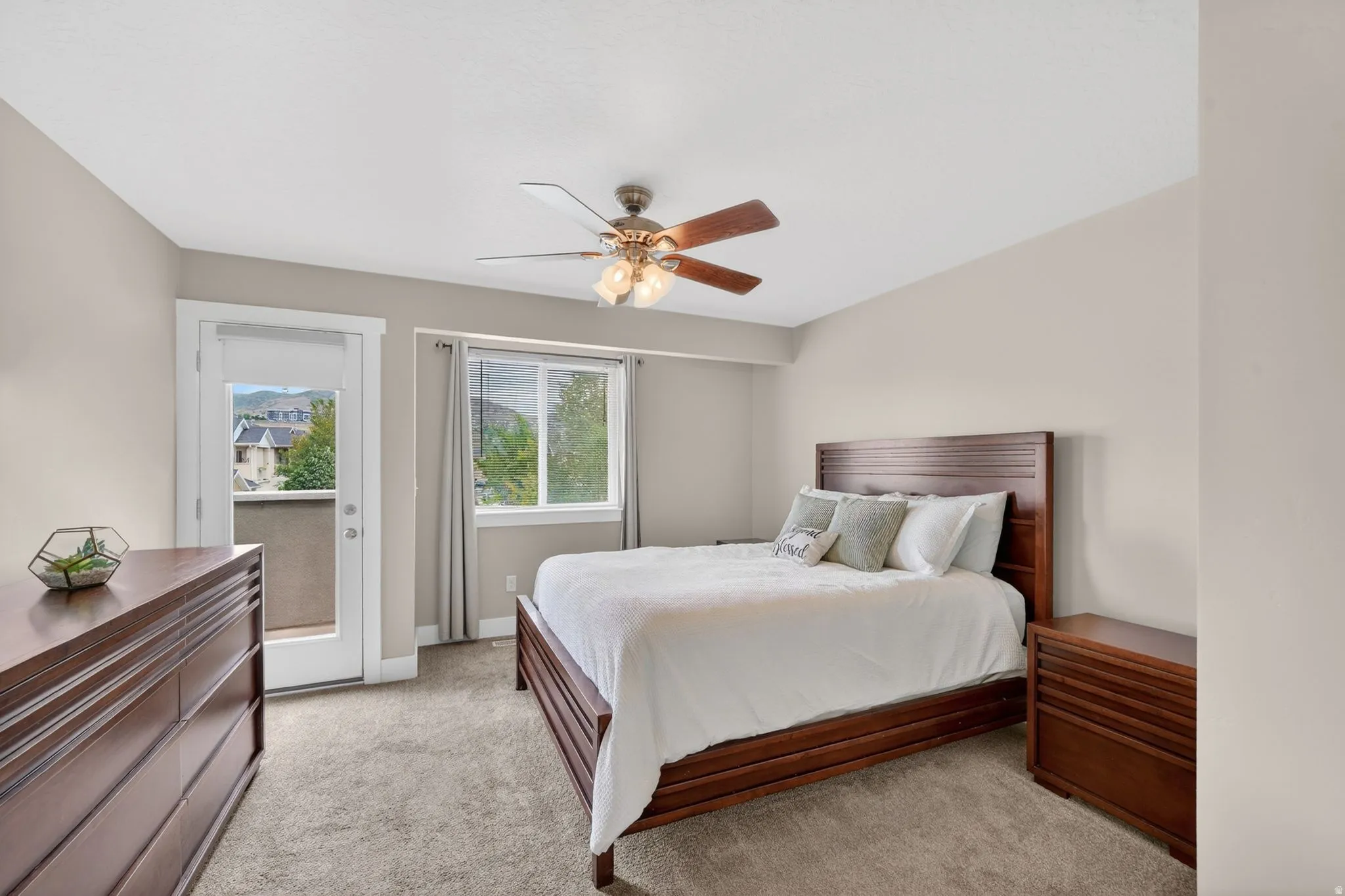 Carpeted bedroom with a private balcony, large window, and a ceiling fan with light fixture