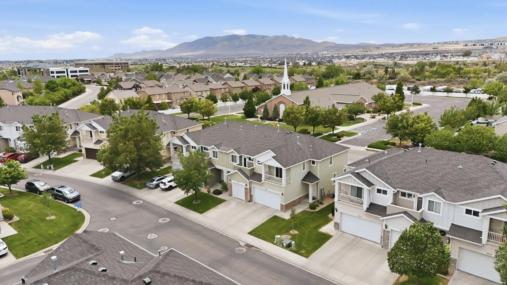 Aerial perspective of a developed residential neighborhood featuring two-story townhomes with attached garages, manicured green spaces, and paved streets