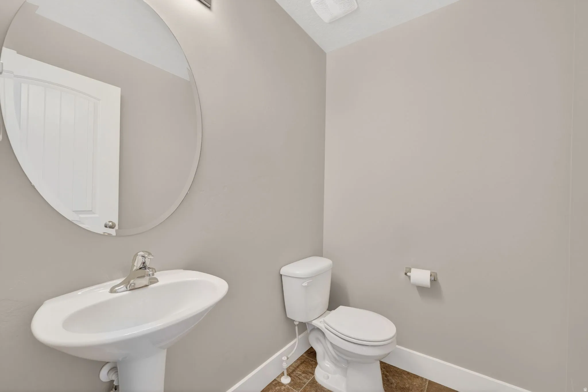 Pedestal sink with chrome faucet, oval mirror, and neutral wall paint