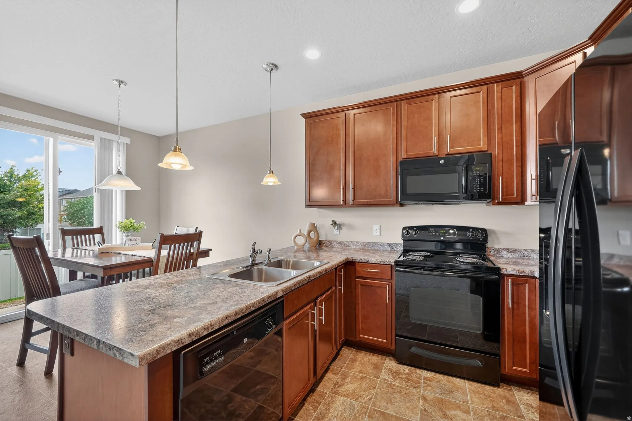 Kitchen featuring wood cabinetry, laminate countertops, a double basin sink, black appliances, and tile flooring