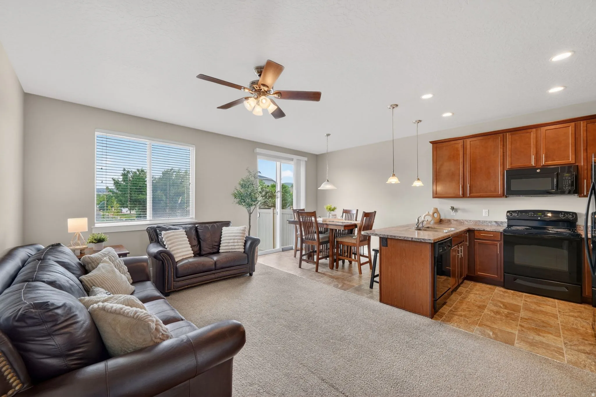 Open-concept living space featuring wood-finish cabinetry, black appliances, a ceiling fan, and sliding glass door