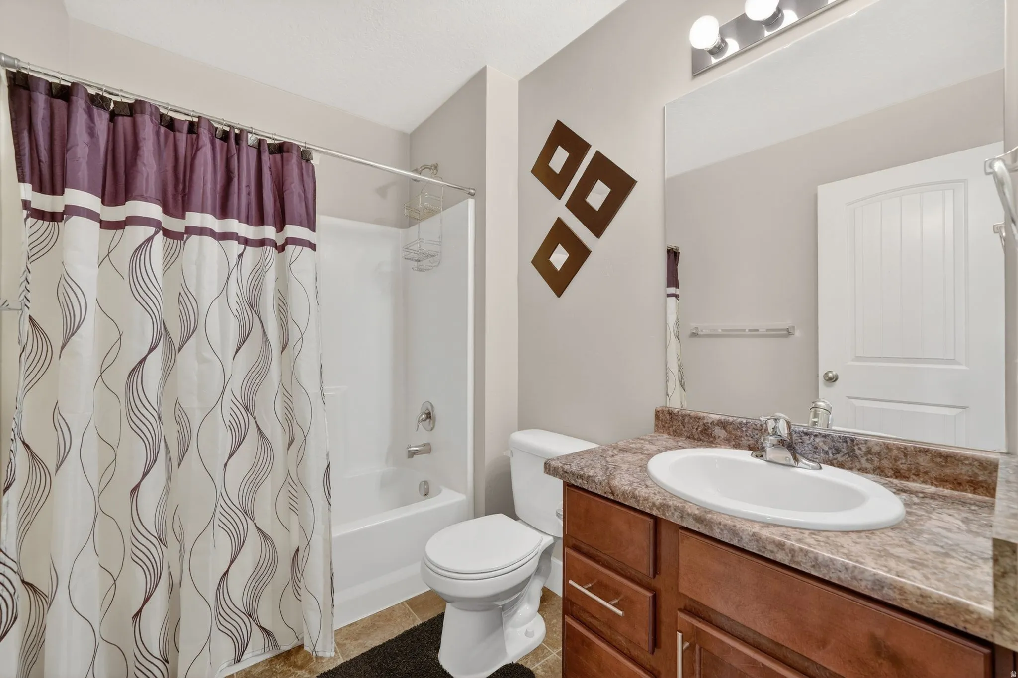 Bathroom featuring a single vanity with a stone-finish countertop, undermount sink, and chrome faucet