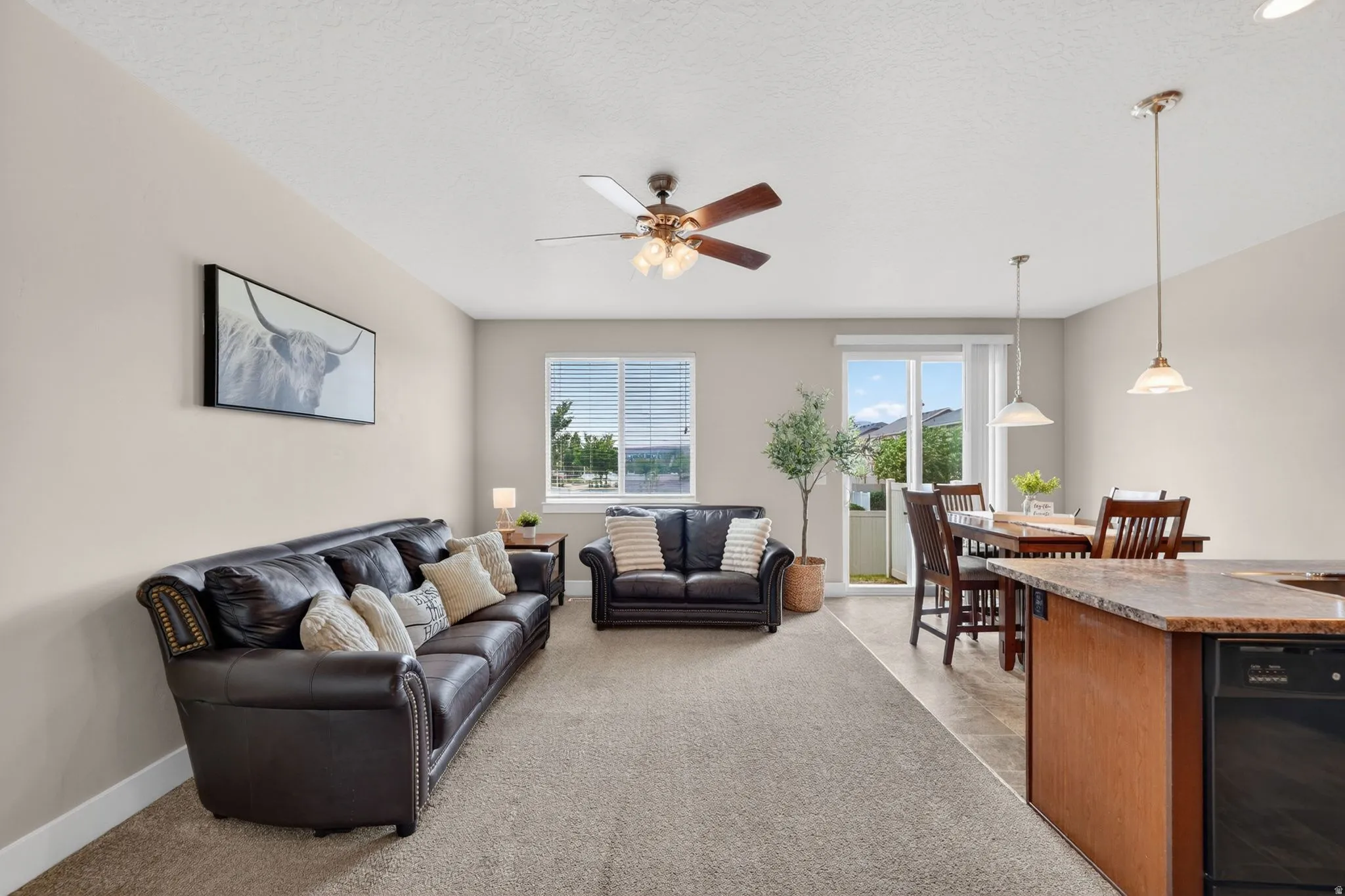 Open-concept living space featuring neutral wall tones, carpeted flooring, and a ceiling fan with integrated lighting