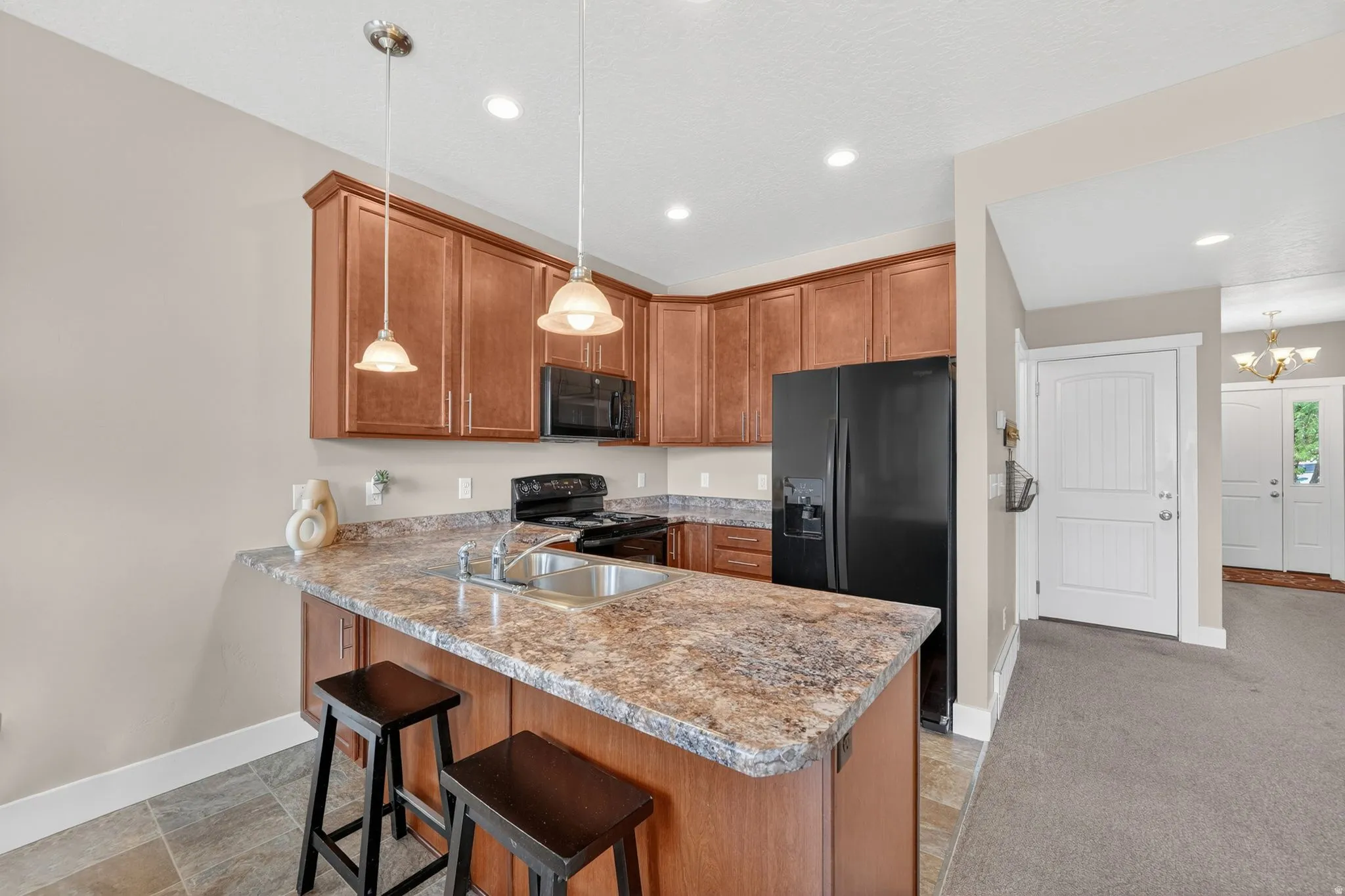 Kitchen featuring wood-finish cabinetry, patterned countertops, and a stainless steel sink with a gooseneck faucet
