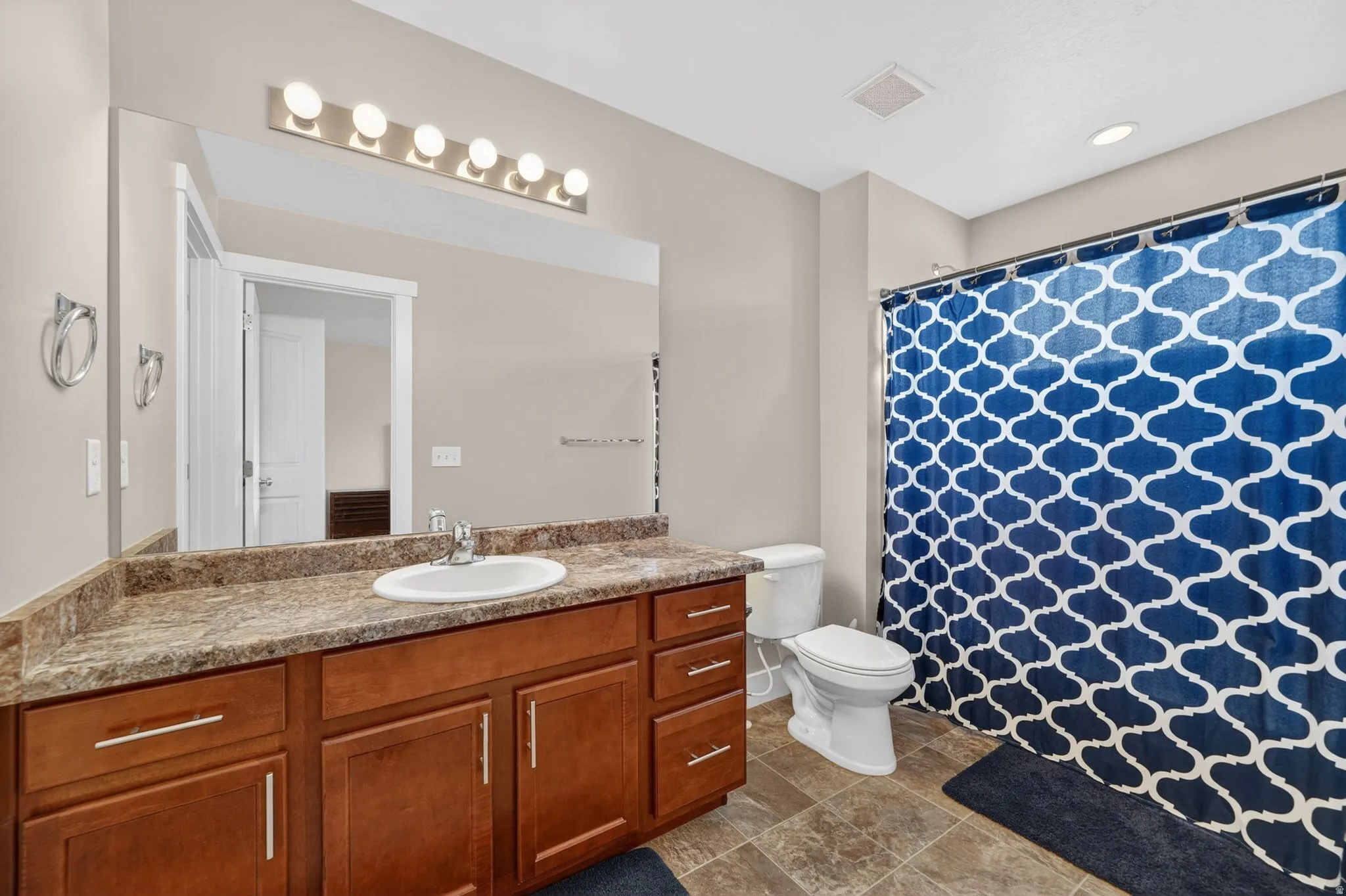 Bathroom featuring a rich wood-tone vanity, a built-in sink, and a spacious mirror with overhead lighting