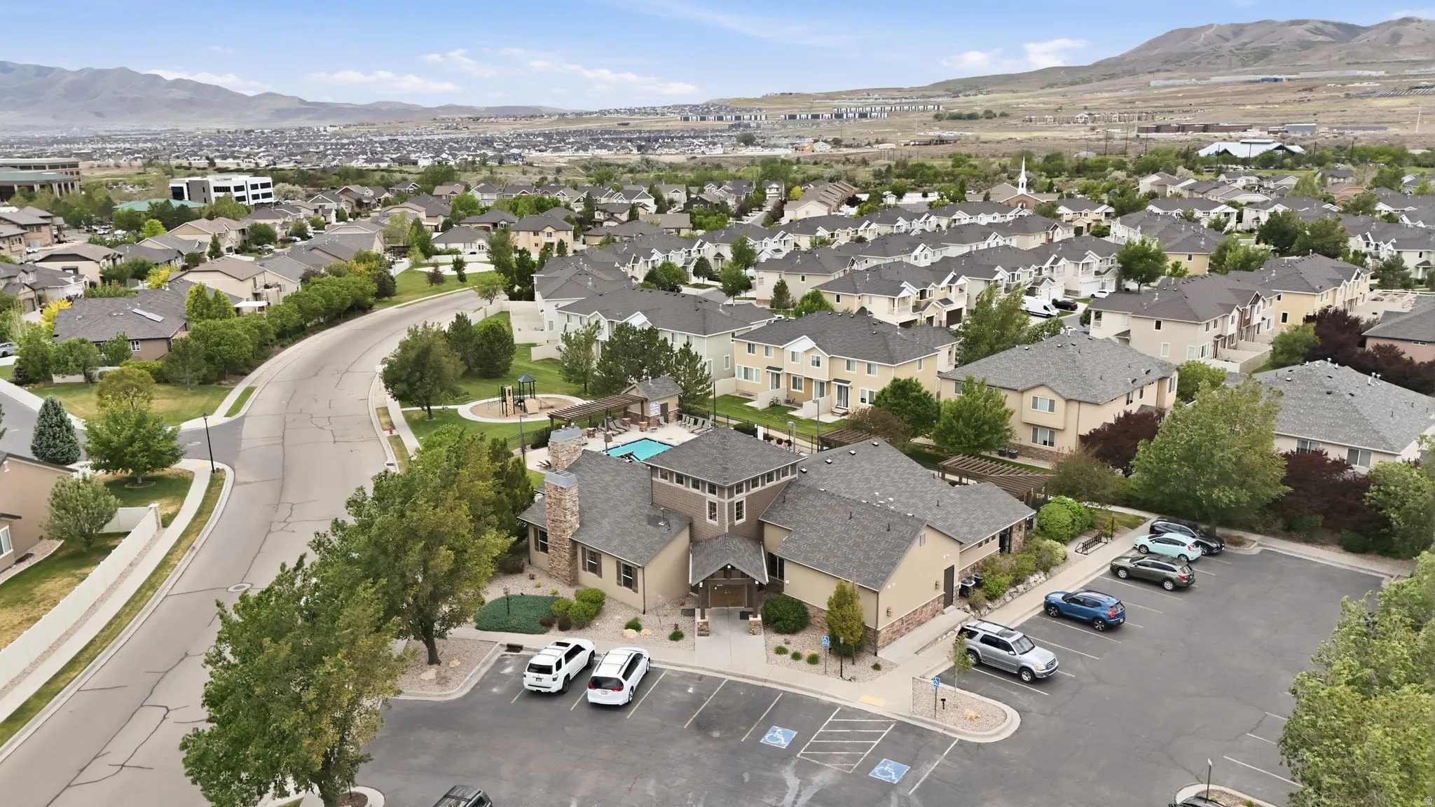 Aerial perspective showcasing a residential community with a central clubhouse building featuring stone and siding exterior finishes, a shingled roof, and an adjacent parking lot