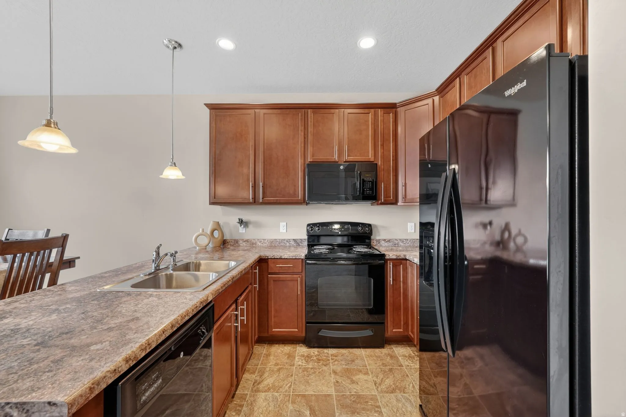 Kitchen featuring wood-finish cabinetry, black appliances, double basin sink, and pendant lighting