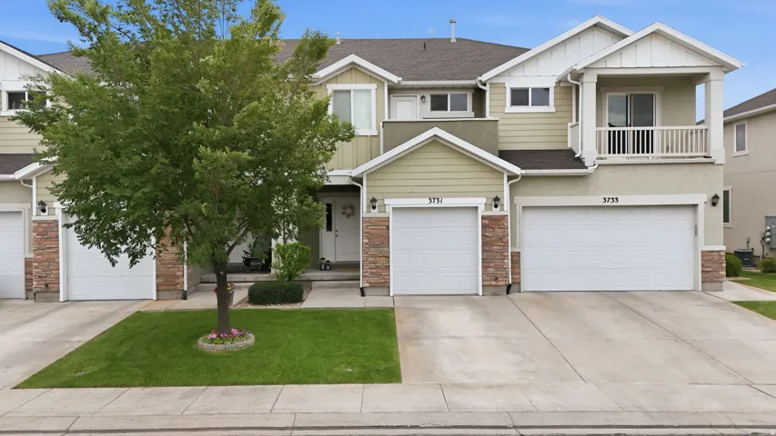 Two-story townhome featuring a balcony, two single-car garages, and a light-toned exterior with stone accents