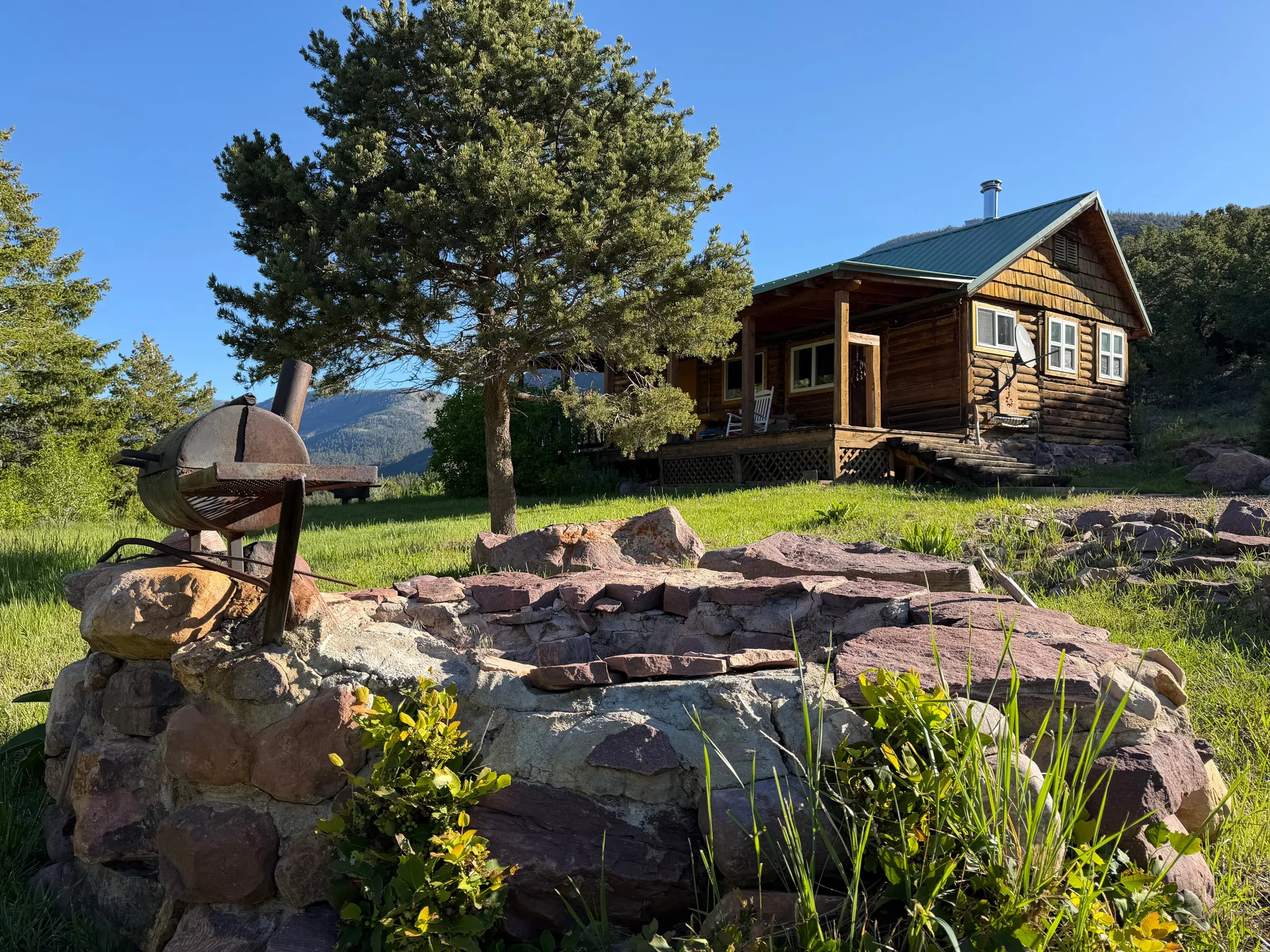 Log cabin exterior featuring a green metal roof, a covered porch, and natural wood siding