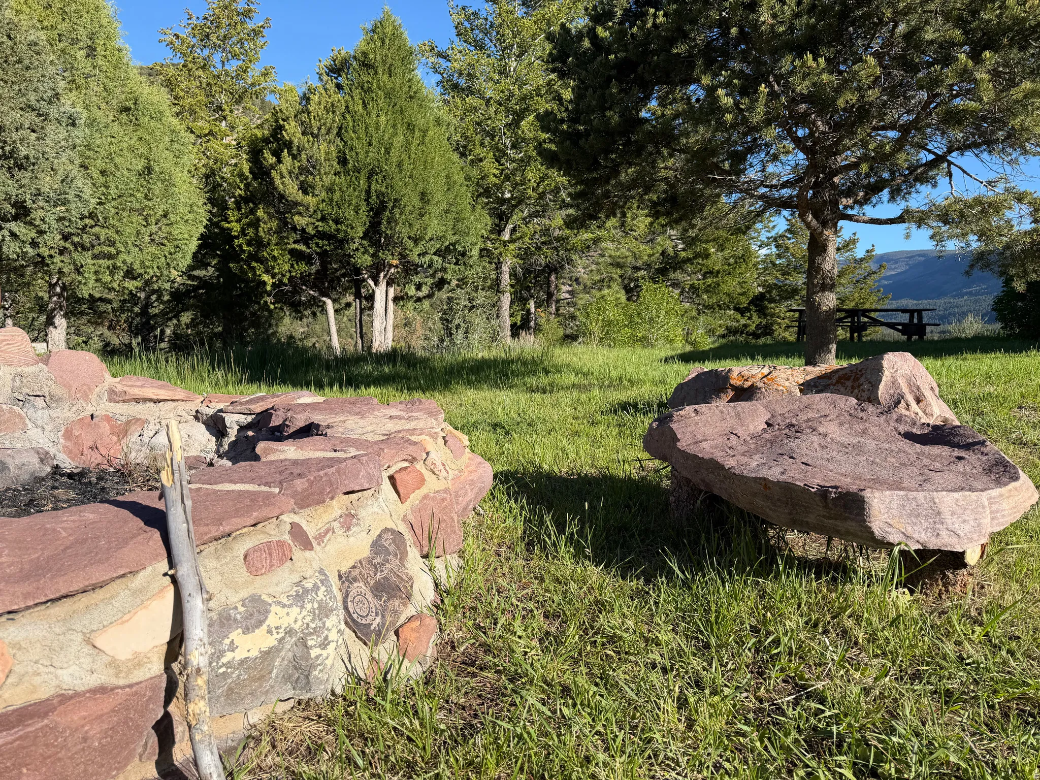 Stone fire pit with natural rock seating and a backdrop of mature trees