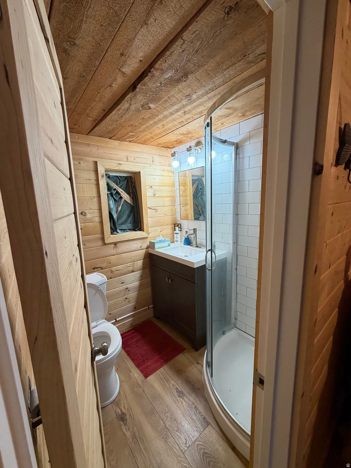 Wood-paneled bathroom featuring a curved glass shower enclosure, a vanity with an integrated sink, wood-finish flooring, and a natural wood plank ceiling