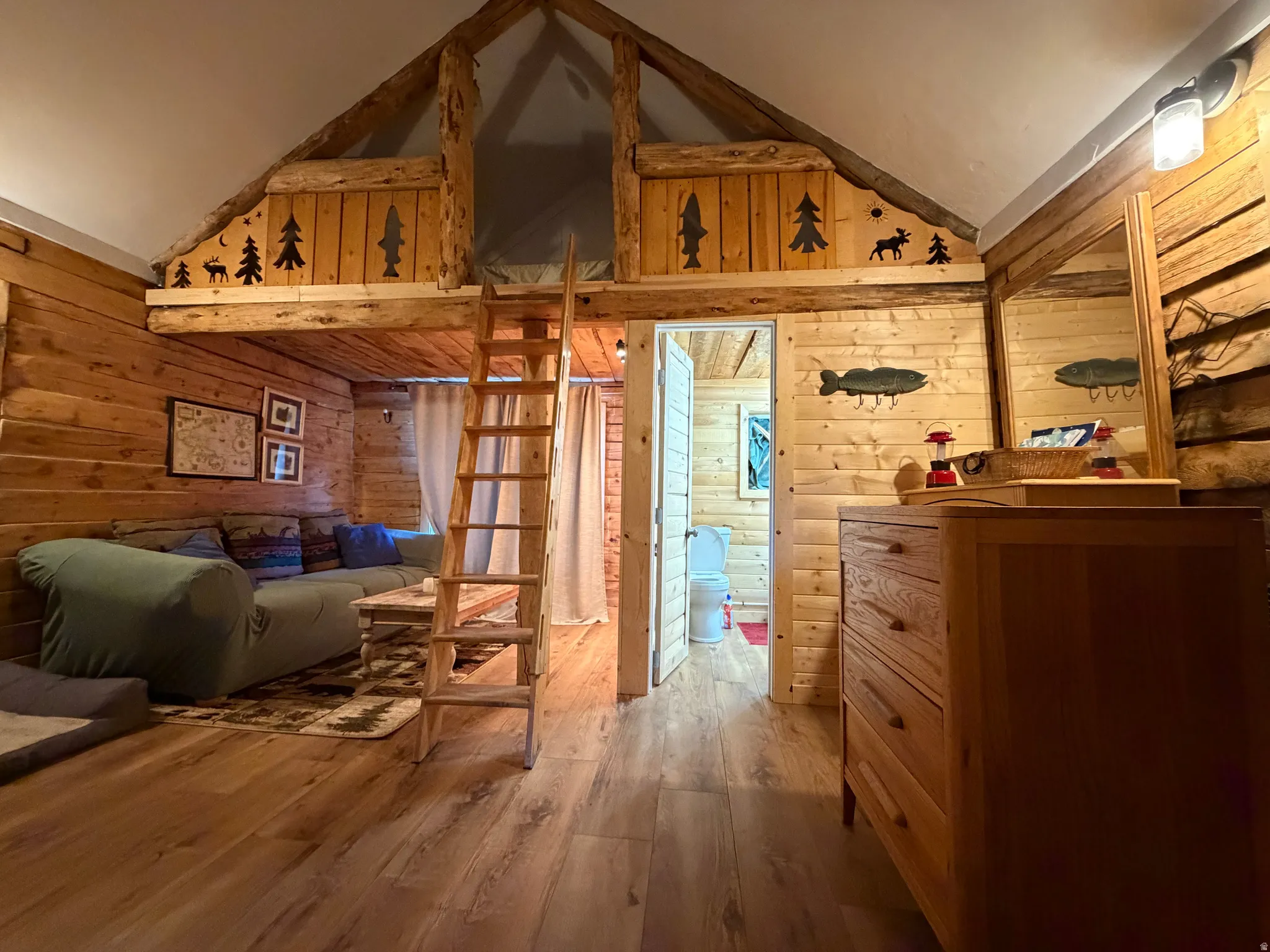Interior space featuring wood-finish flooring, natural wood paneling, an exposed beam ceiling, a wooden ladder providing access to an upper loft, and a doorway opening to another room