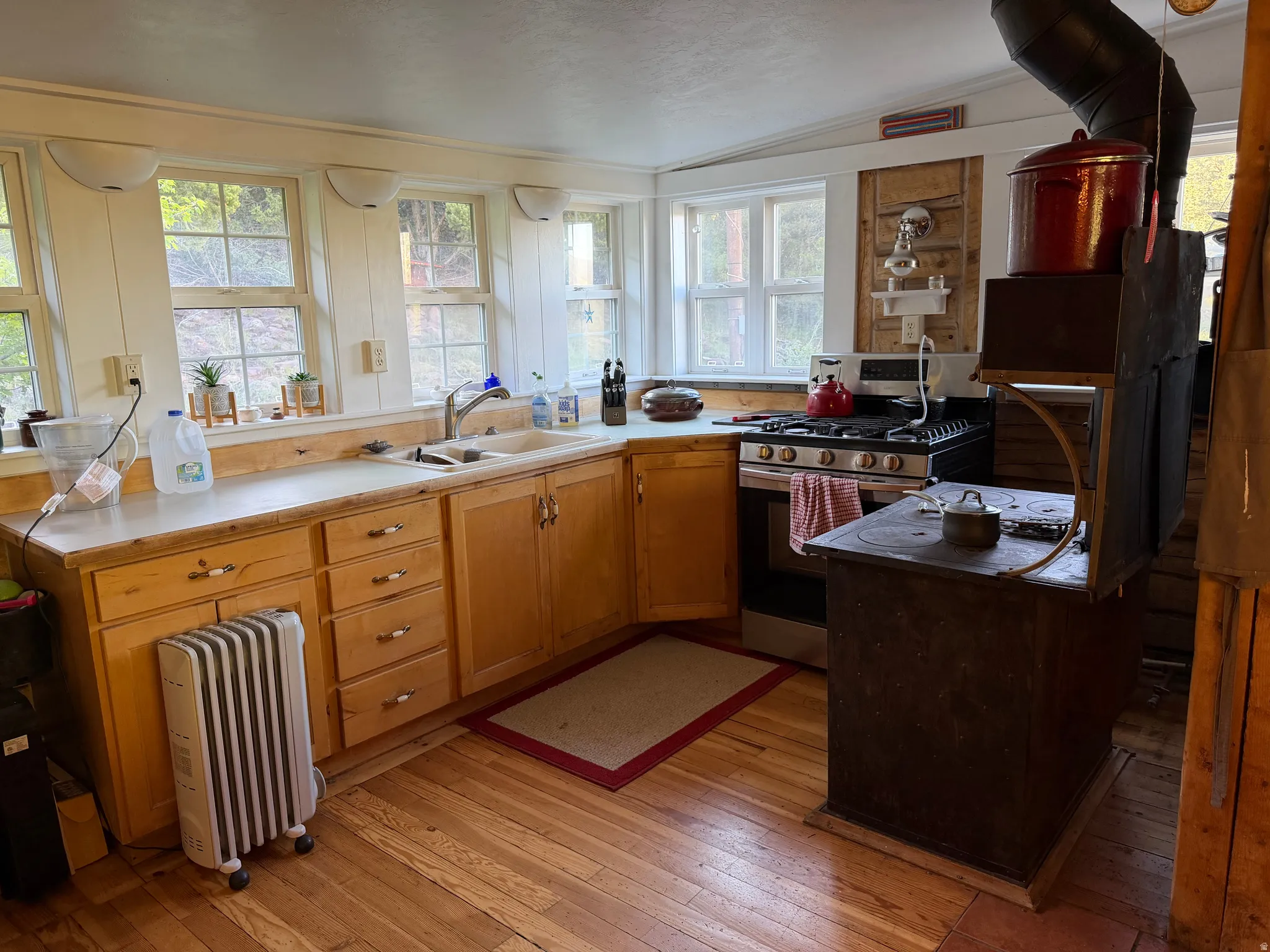Kitchen featuring warm wood-finish flooring, light wood cabinetry with varied drawer and door configurations, a stainless steel range, and a built-in antique-style wood-burning cookstove