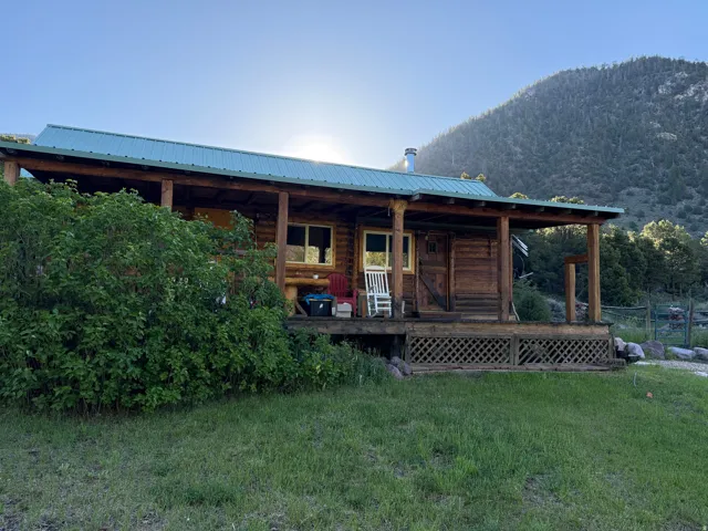 Log cabin exterior featuring a covered porch, a green metal roof, and a visible chimney