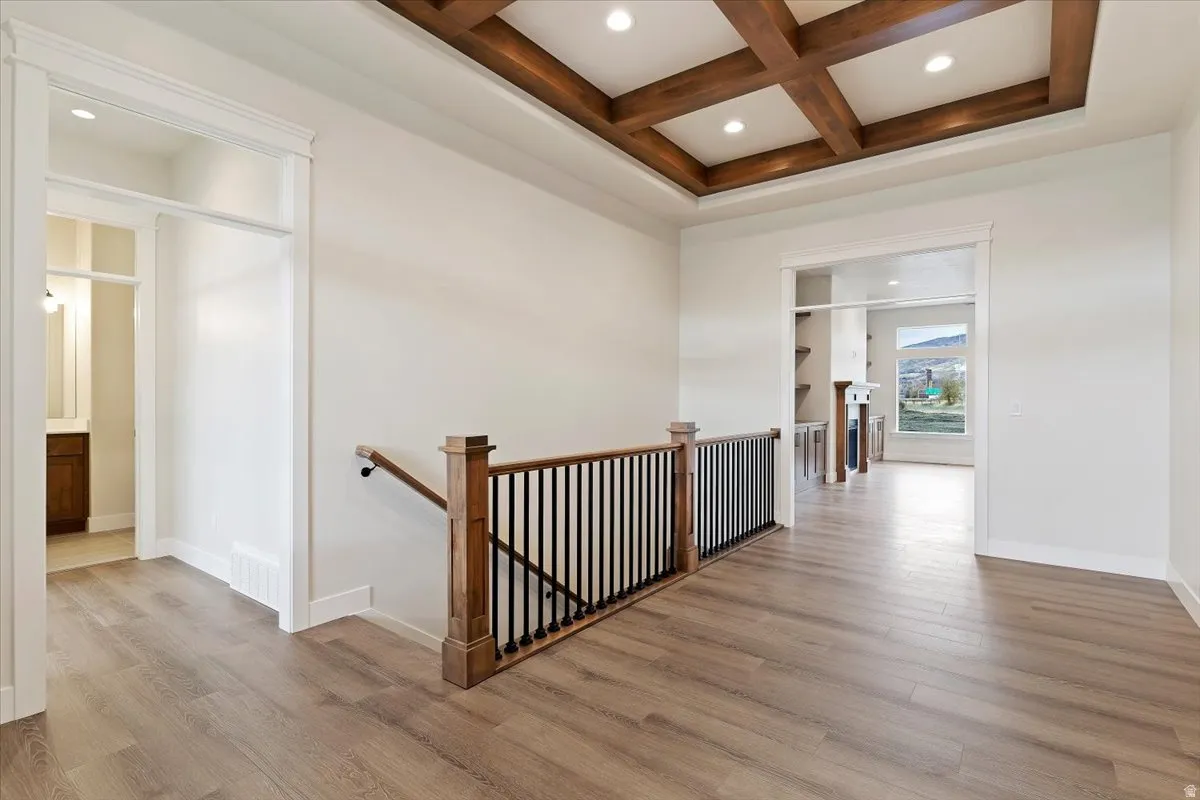 Exposed coffered ceiling with recessed lighting, LVP flooring, and a decorative staircase railing with black iron balusters