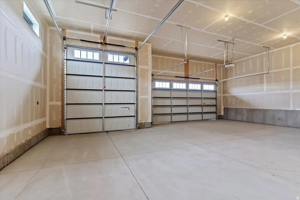Spacious garage featuring two overhead doors with transom windows, a concrete floor, and unpainted drywall