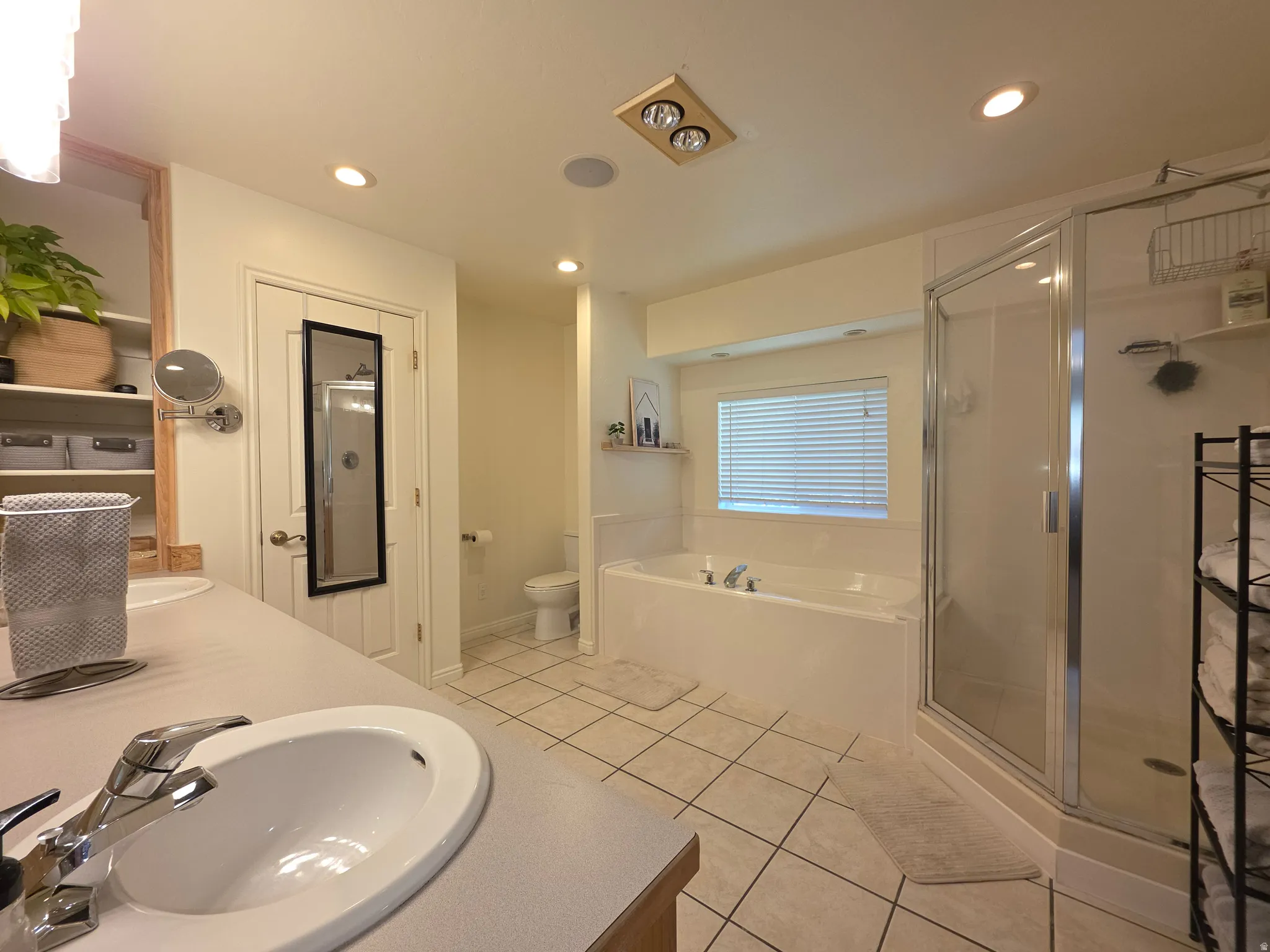 Spacious bathroom featuring a dual vanity, built-in shelving, a glass-enclosed shower, a deep soaking tub, and tiled flooring