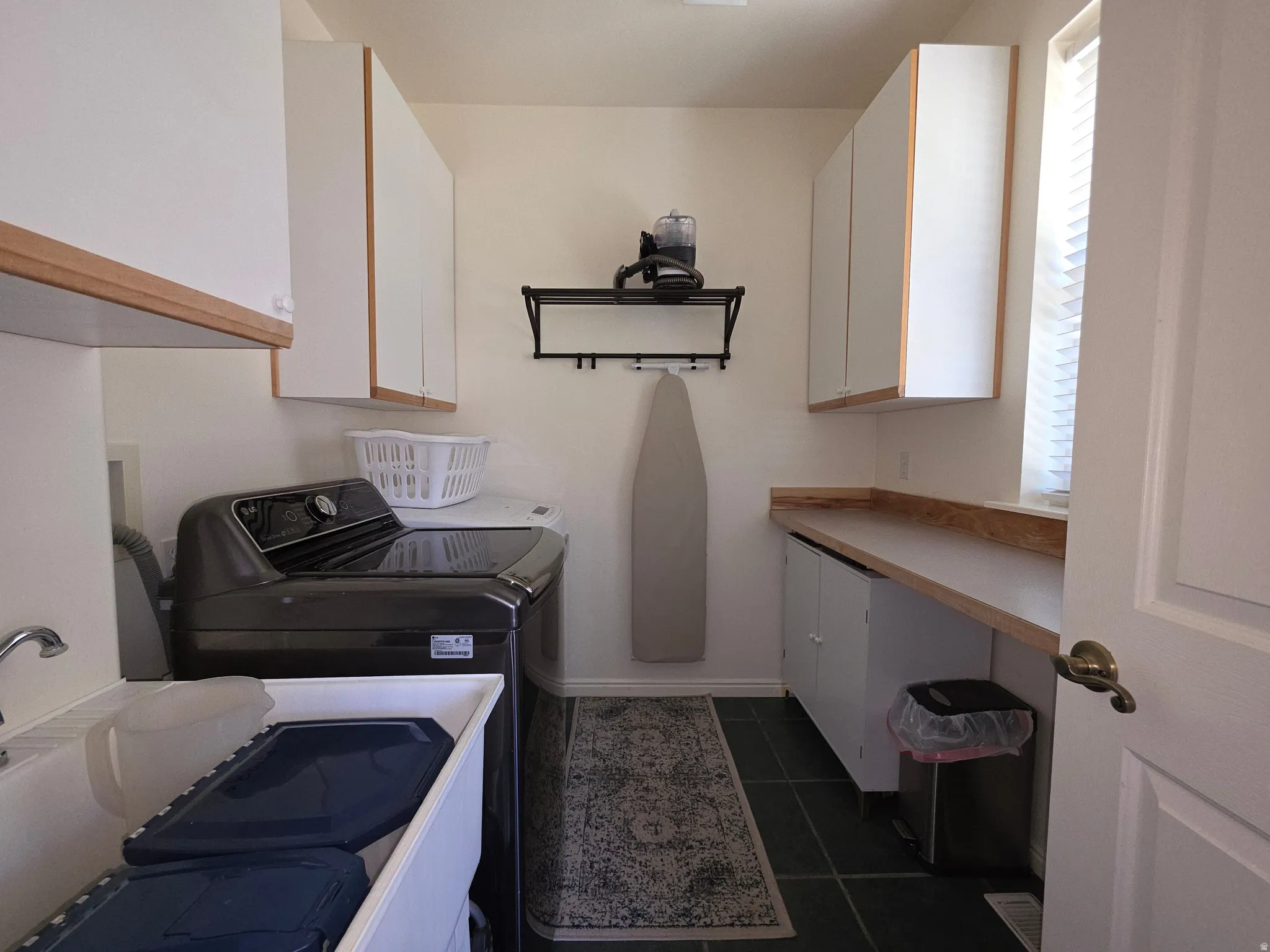Dedicated laundry room featuring tile flooring, white cabinetry with wood-finish trim, and a window for natural light