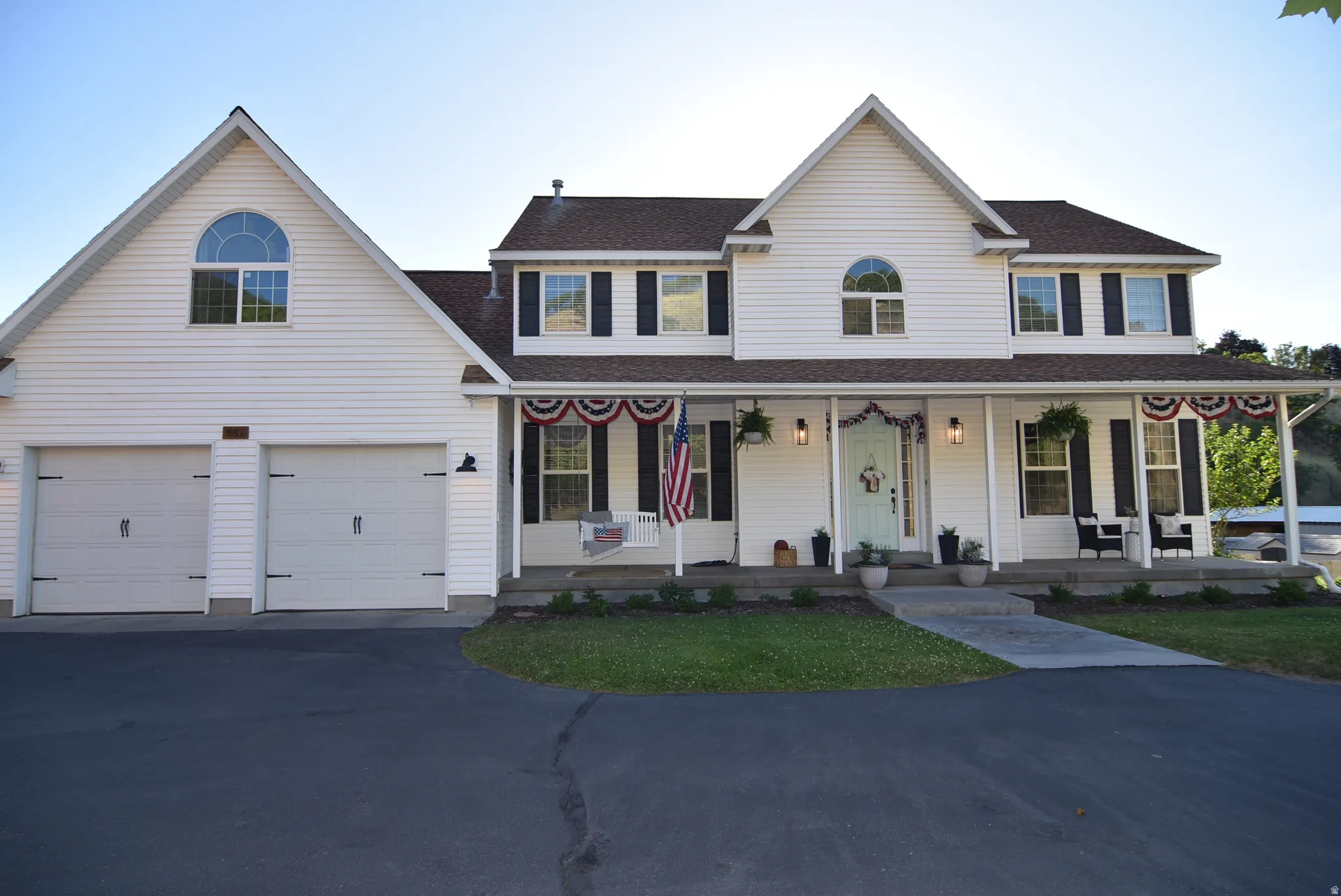 Two-story home featuring a full-width covered porch, white siding, and a two-car garage