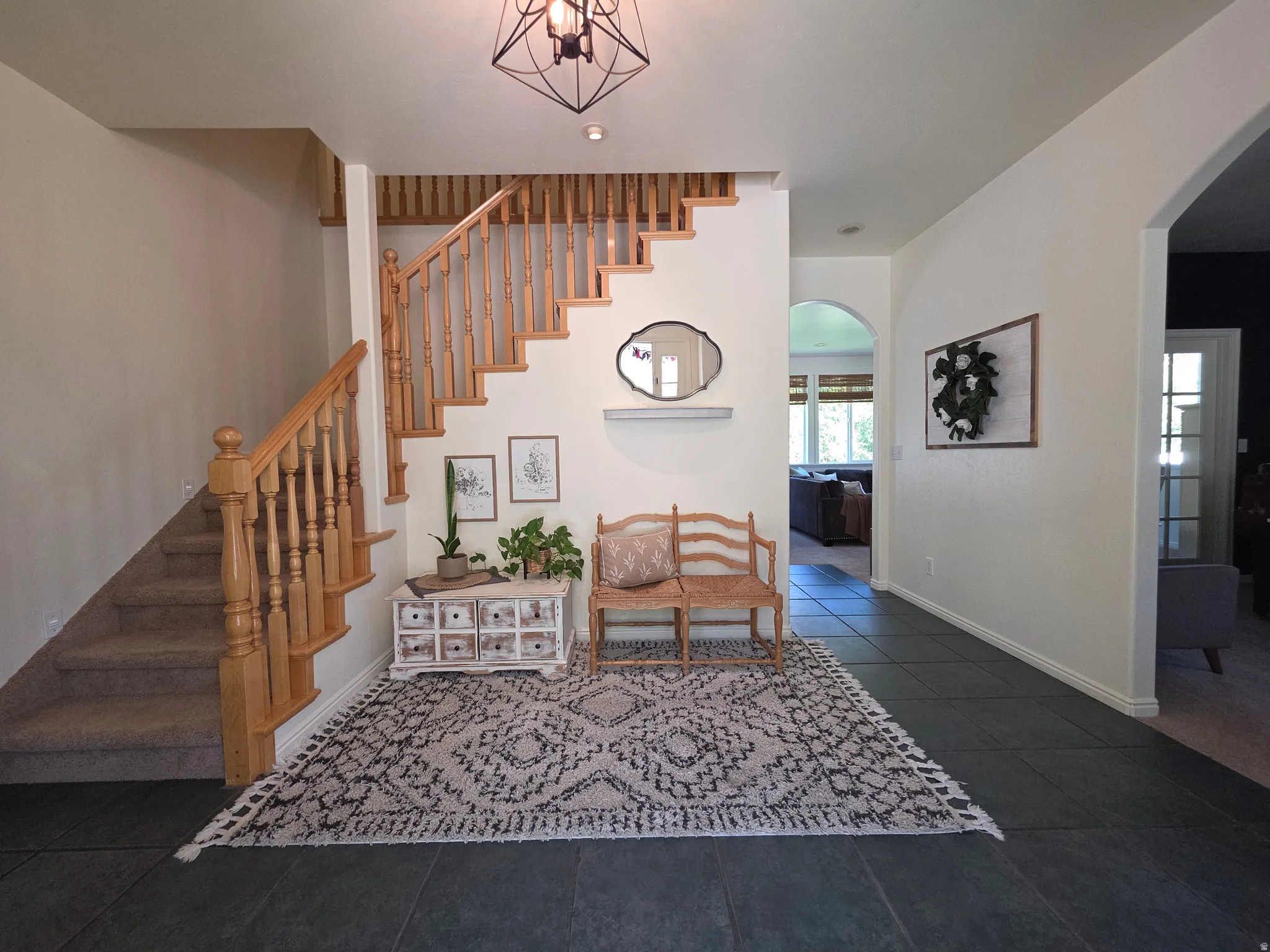 Inviting entryway featuring a wood staircase with carpeted treads, dark tile flooring, and arched doorways