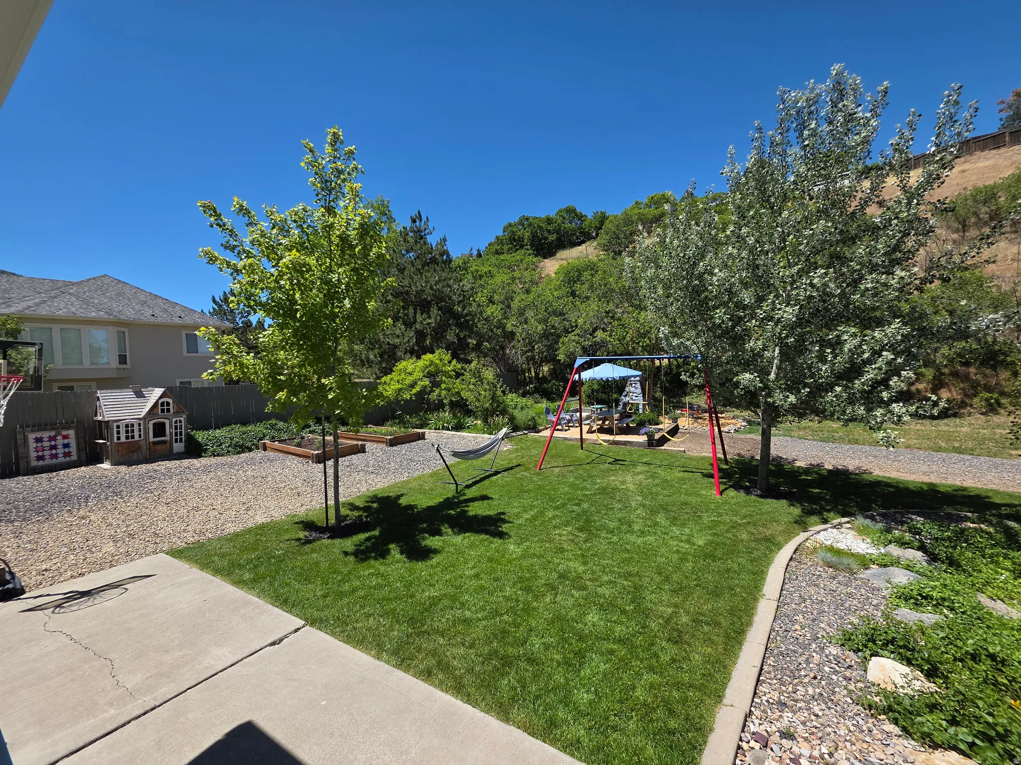 Expansive backyard featuring a vibrant green lawn, mature trees, a gravel patio area, and raised garden beds
