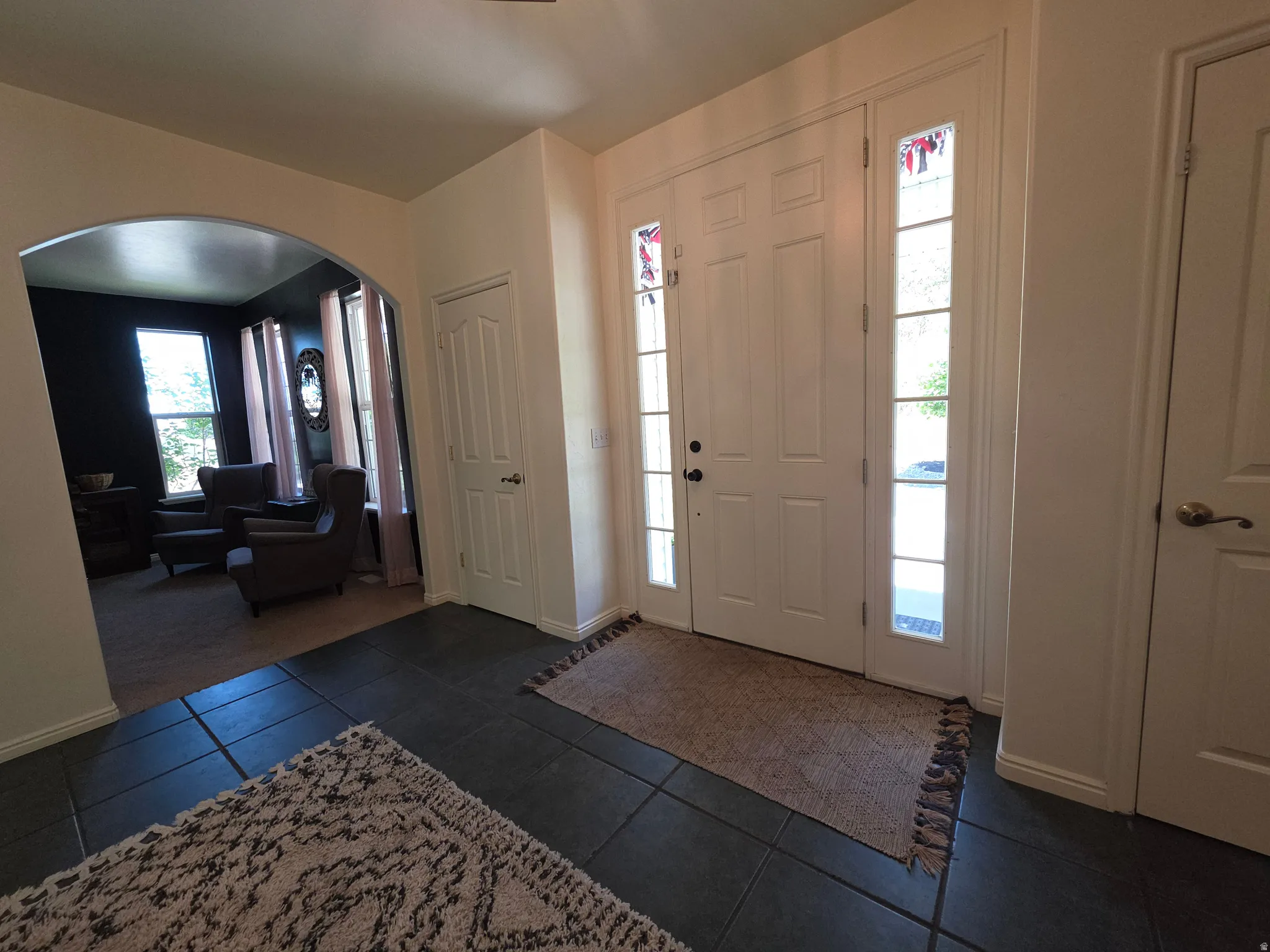 Entryway featuring white paneled double doors with clear glass sidelights, dark tile flooring, and light-toned walls