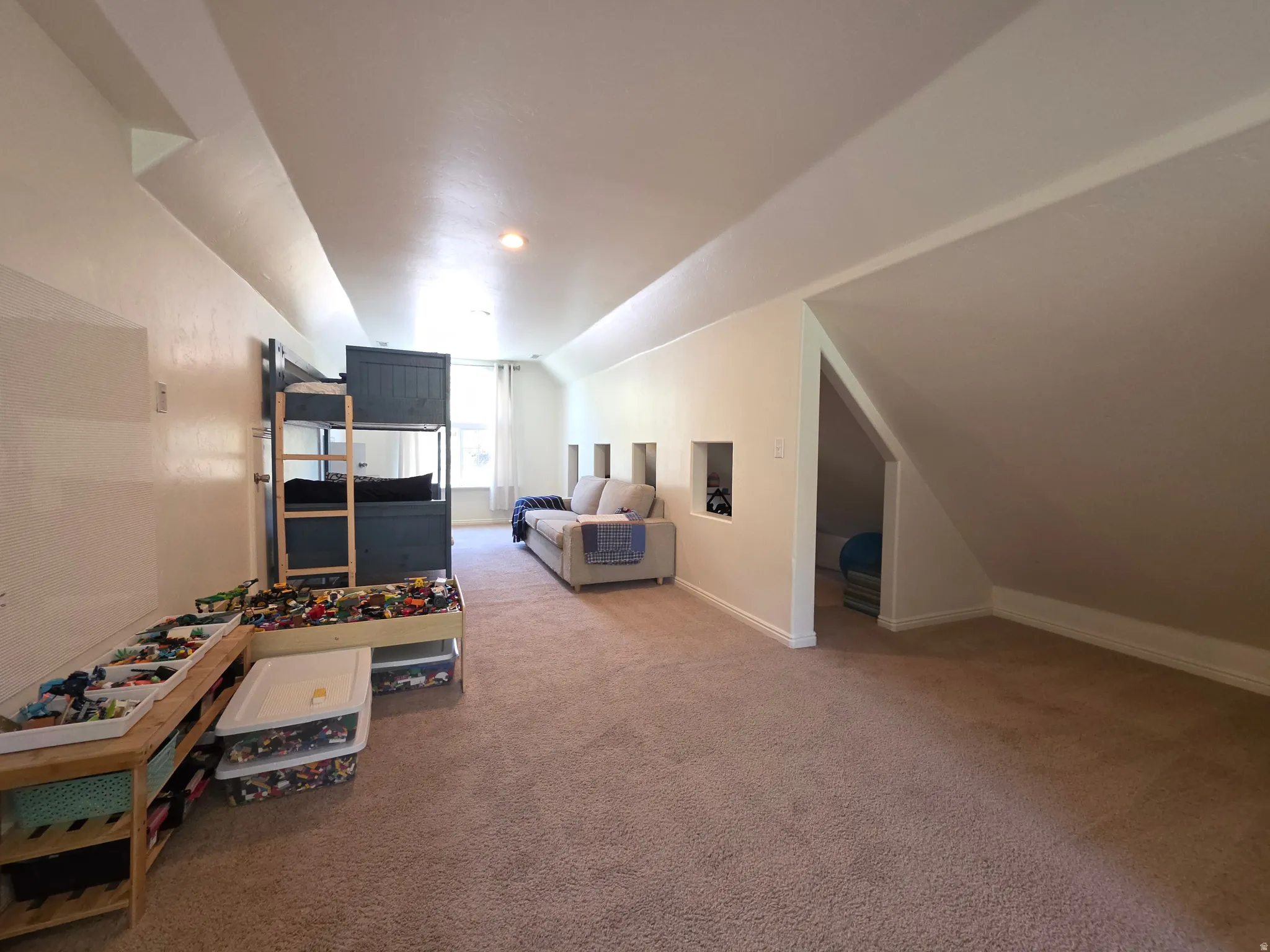 Spacious room featuring sloped ceilings, recessed wall niches, a built-in bunk bed, and plush carpet flooring