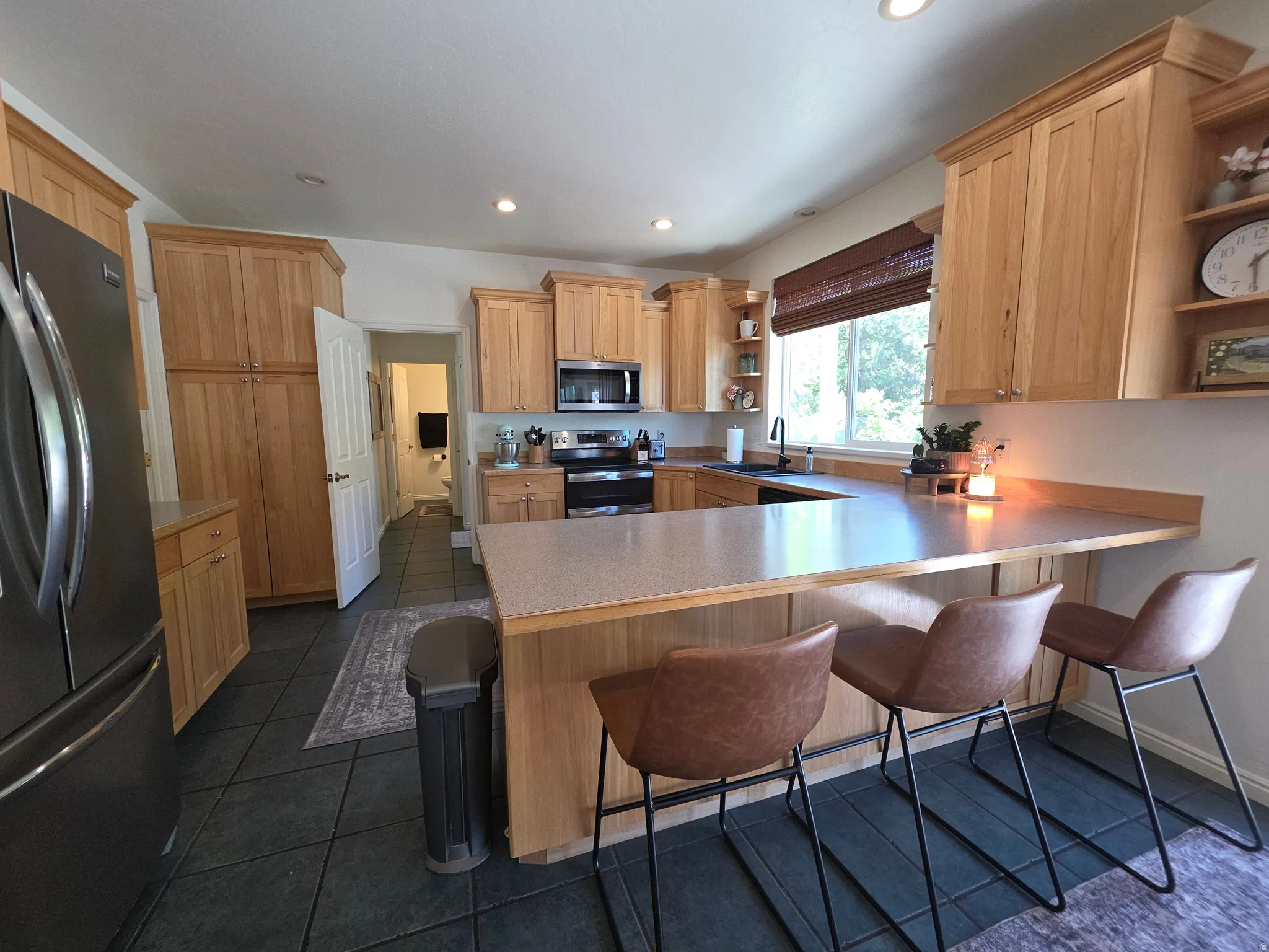 Spacious kitchen featuring extensive light wood cabinetry, black tile flooring, stainless steel appliances, a generous island with seating, and recessed lighting