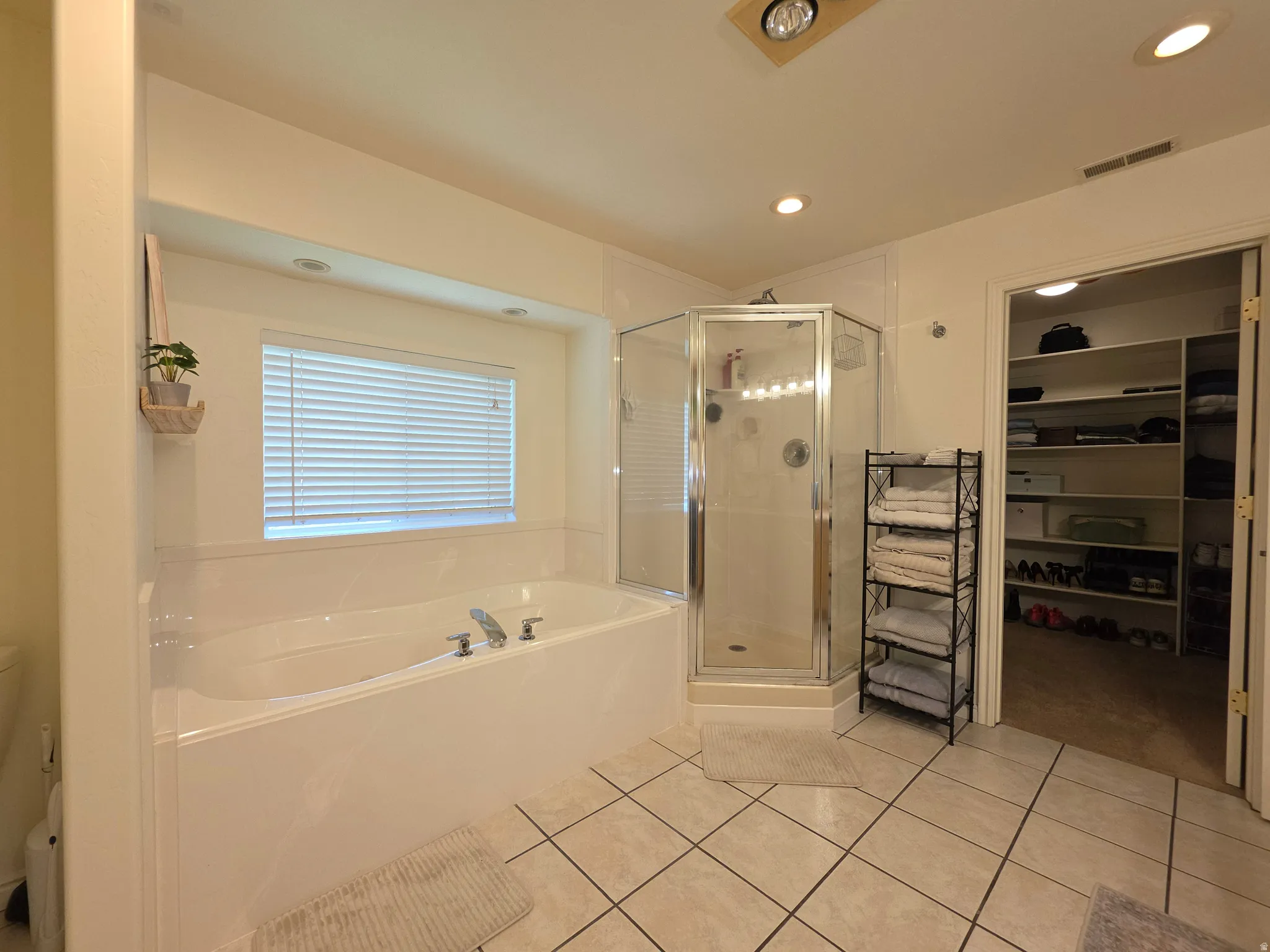 Spacious bathroom featuring a built-in soaking tub, separate glass-enclosed shower, ceramic tile flooring, and recessed lighting