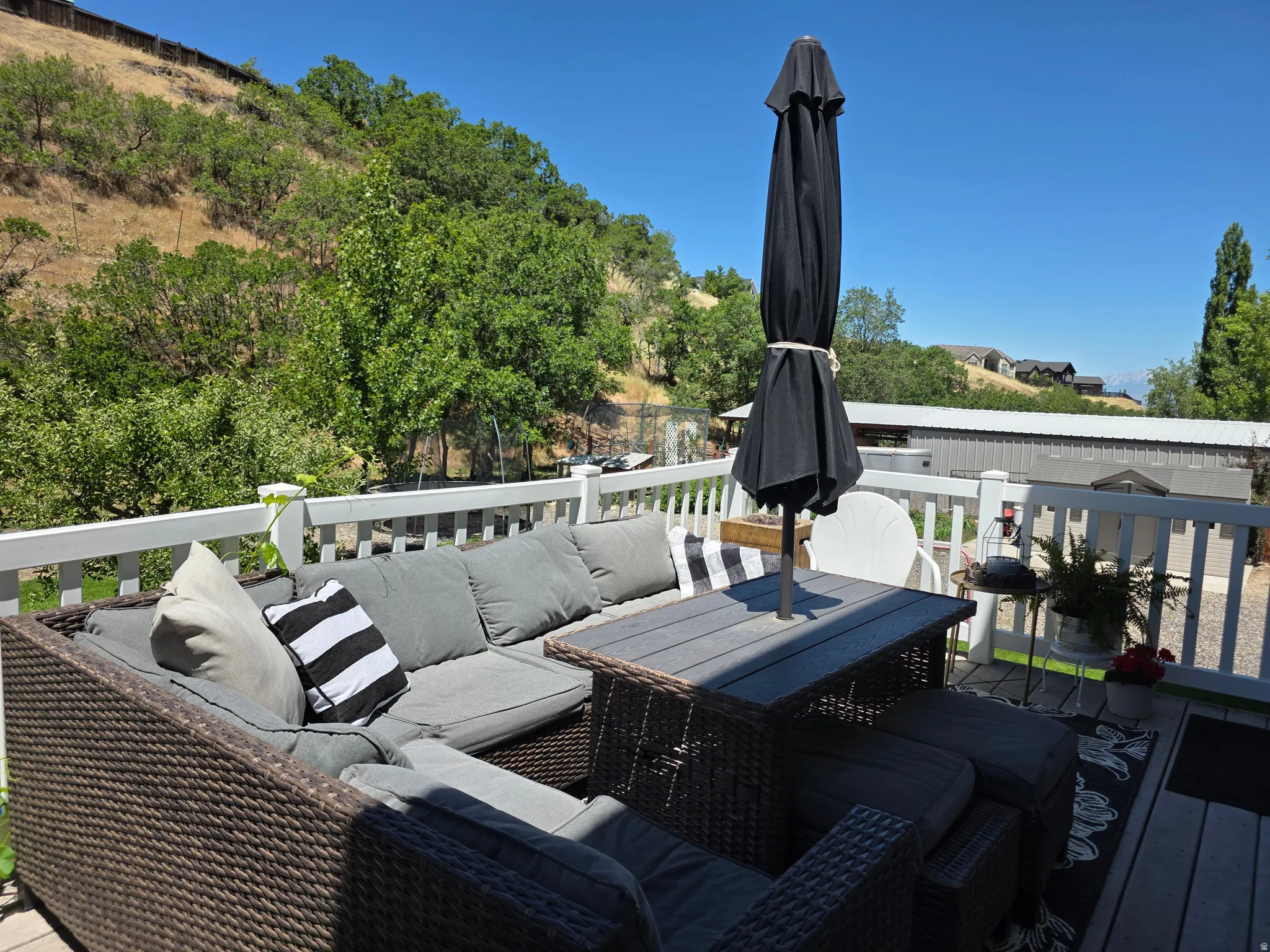 Spacious outdoor deck featuring light-colored railing, gray composite decking, and a backdrop of green foliage and distant hills