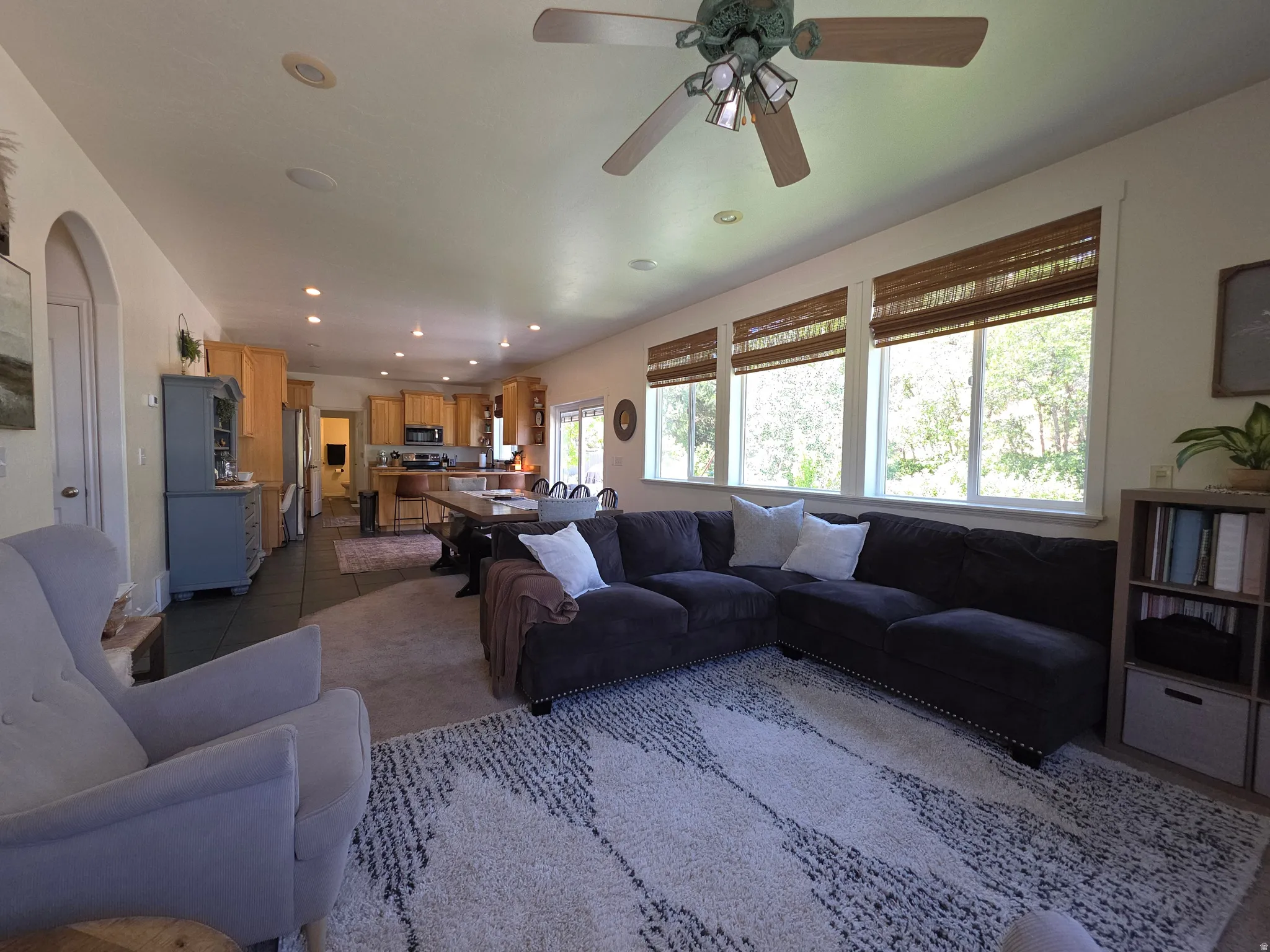 Spacious open-concept living area featuring a row of multiple windows with woven blinds, recessed lighting, and a ceiling fan