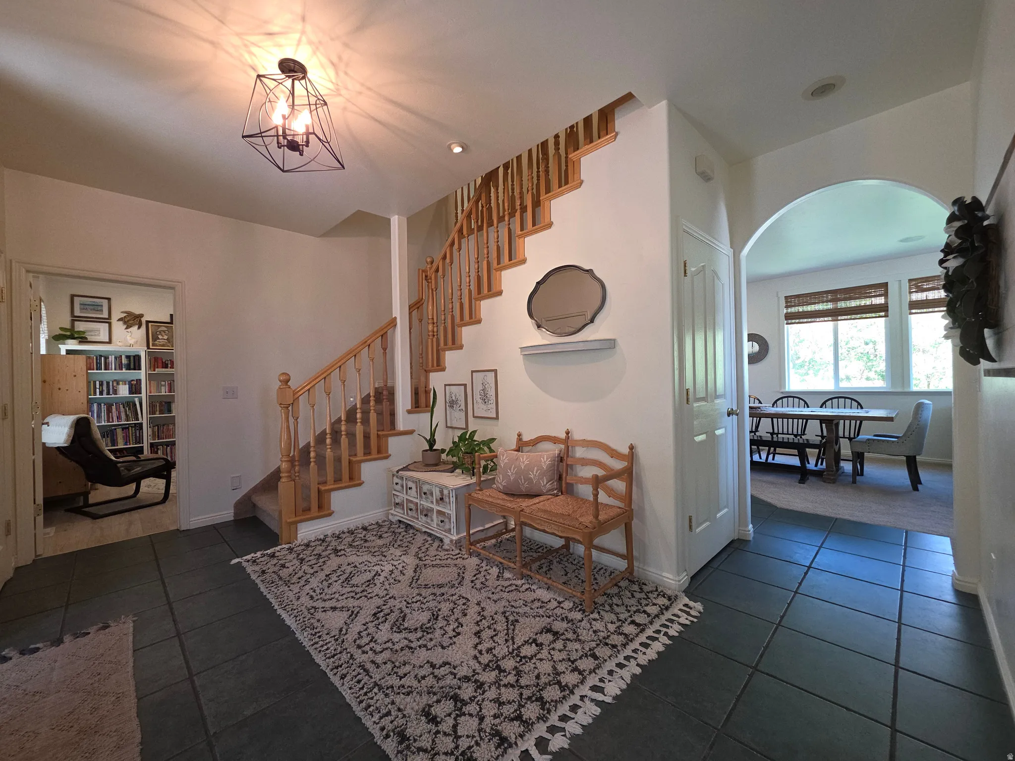 Entryway featuring dark square floor tiles, a staircase with wood balusters and handrail, and an arched doorway
