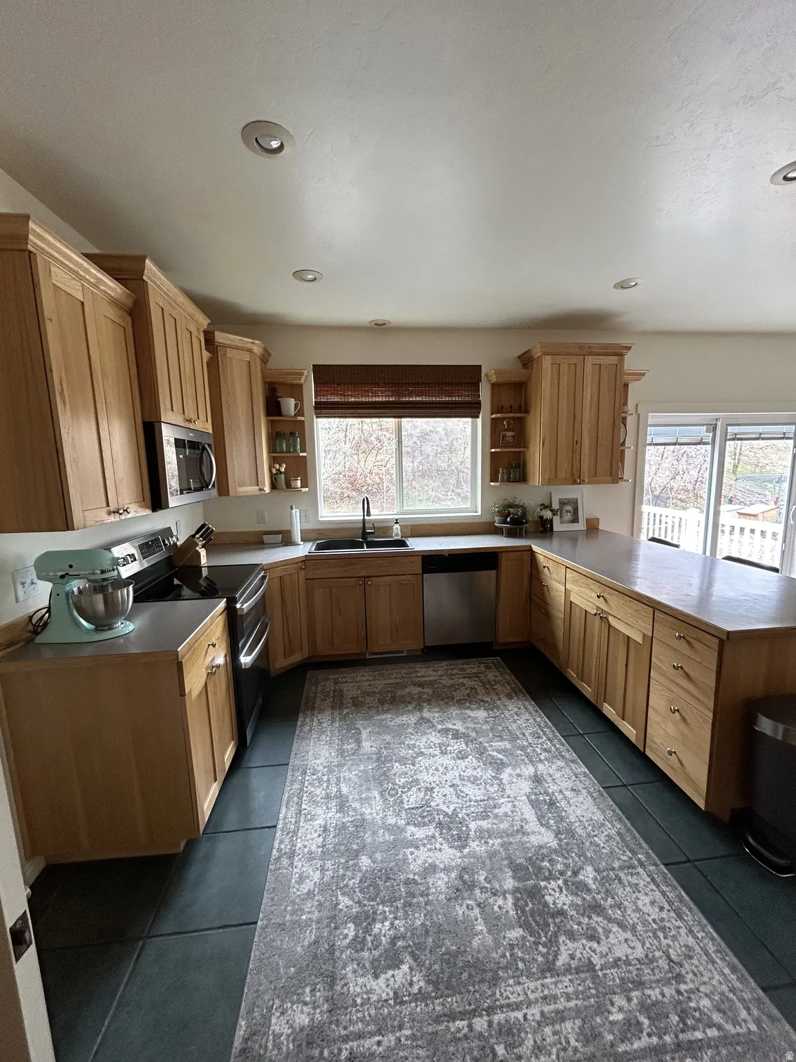 U-shaped kitchen featuring wood-finish cabinetry, dark countertop surfaces, and stainless steel appliances
