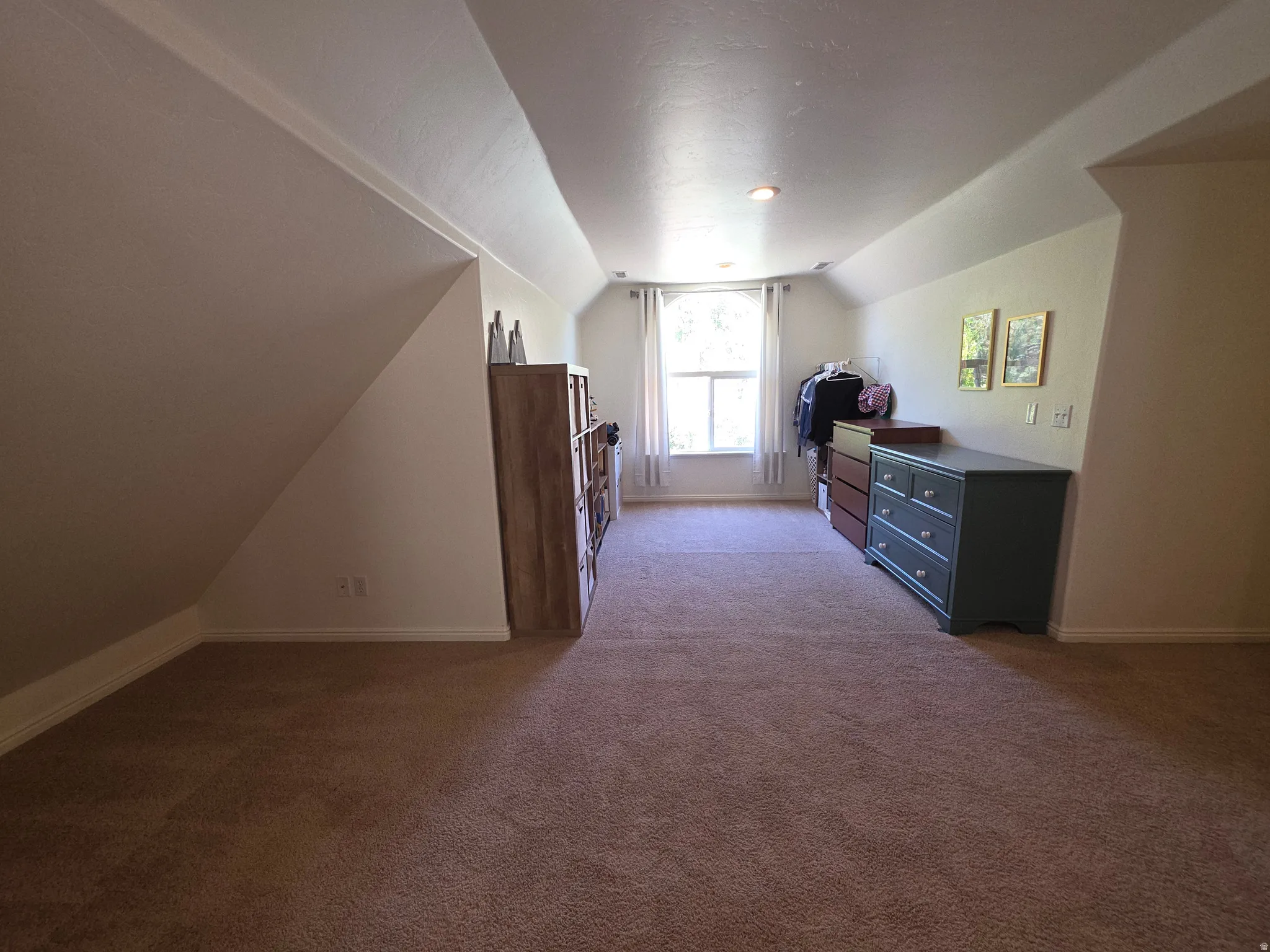 Carpeted room featuring a window with white trim, sloped ceiling lines, and recessed lighting