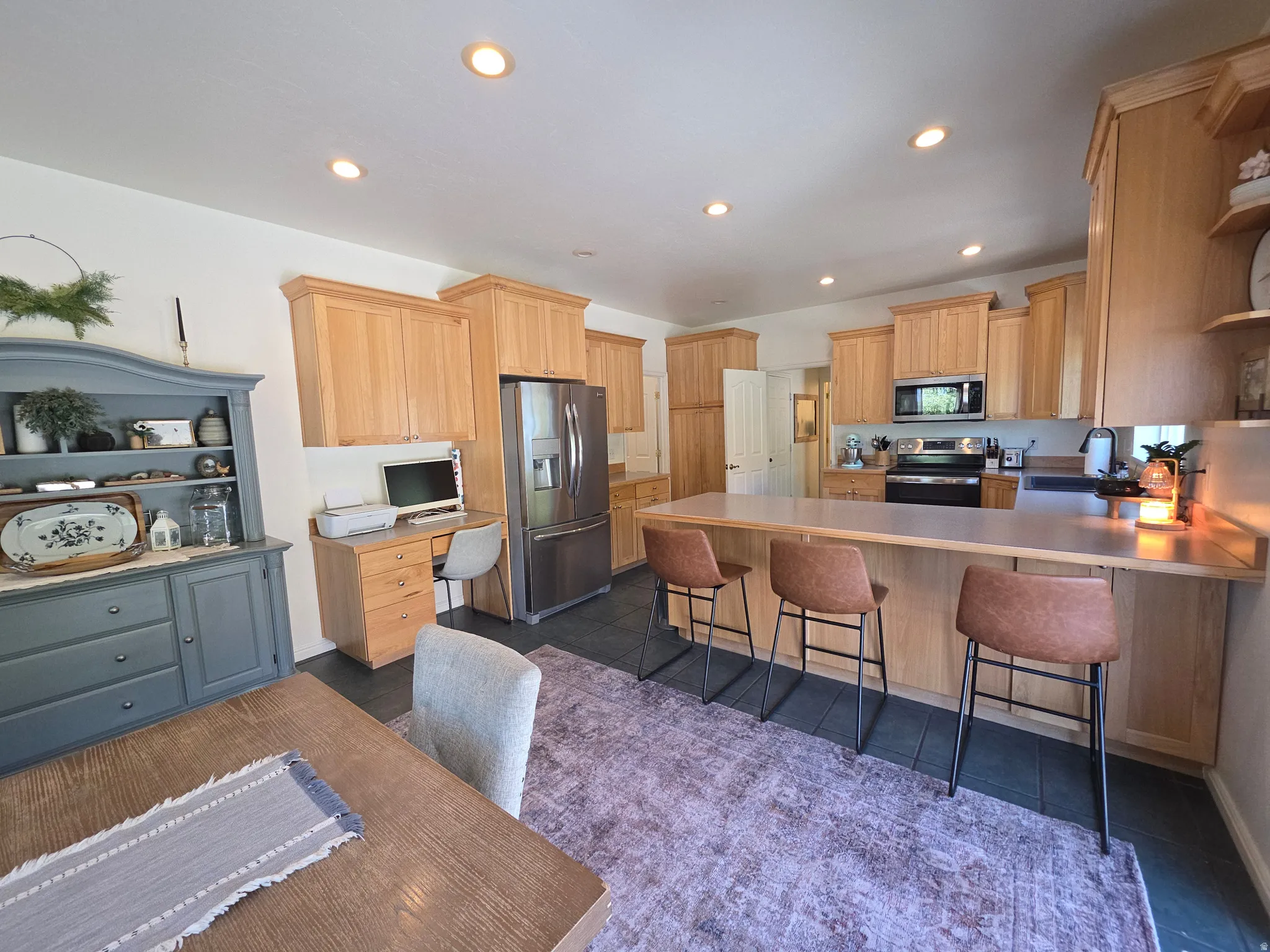Kitchen featuring wood-finish cabinetry, stainless steel appliances, recessed ceiling lighting, a built-in desk area, and an expansive breakfast bar