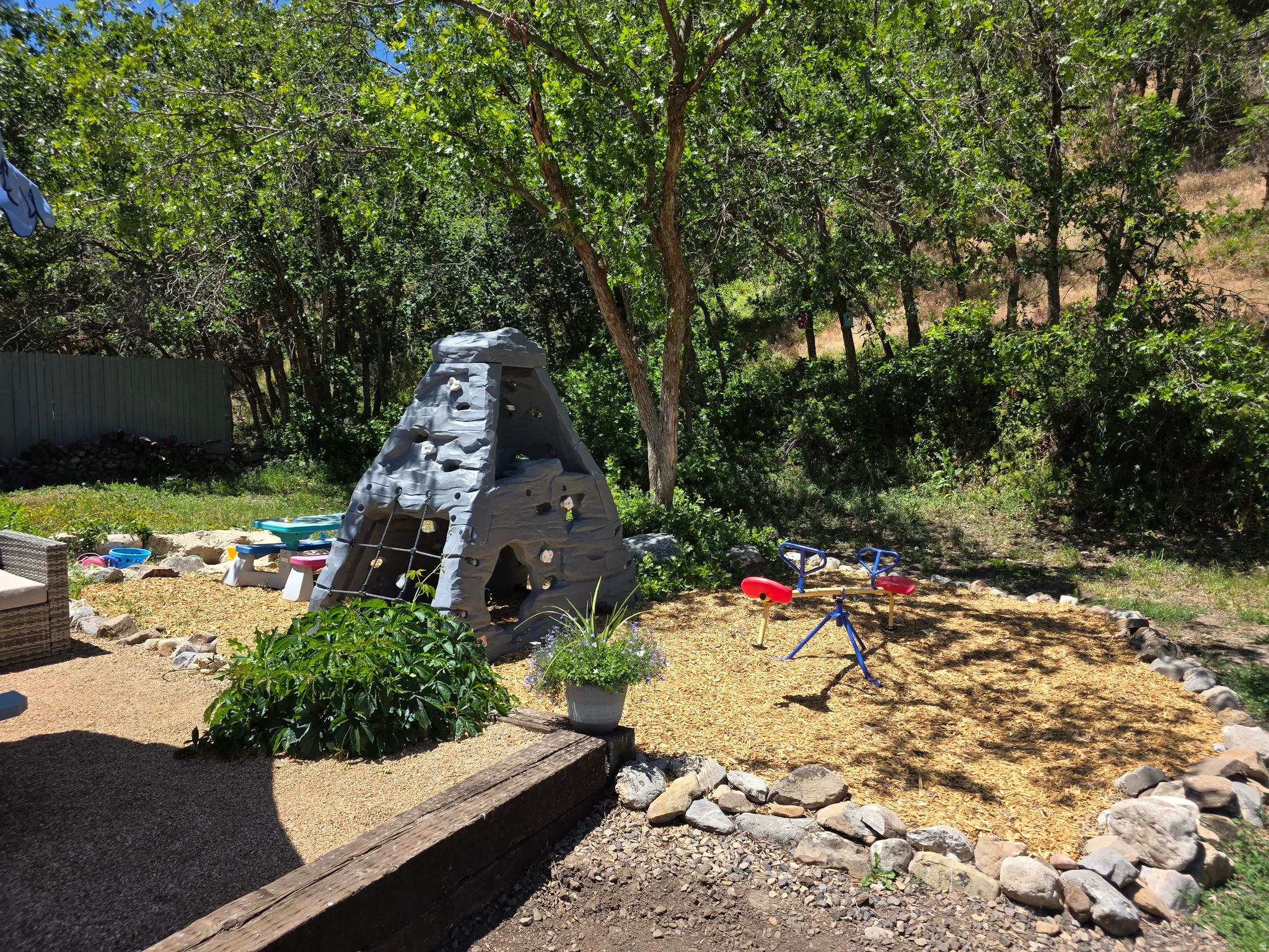 Backyard play area featuring a climbing structure, wood chip ground cover, and a rustic timber retaining wall