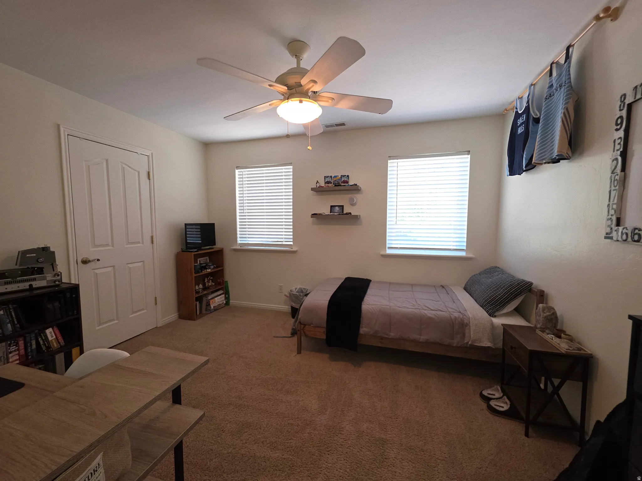 Carpeted room featuring a ceiling fan with integrated lighting, a paneled interior door, and two windows with horizontal blinds