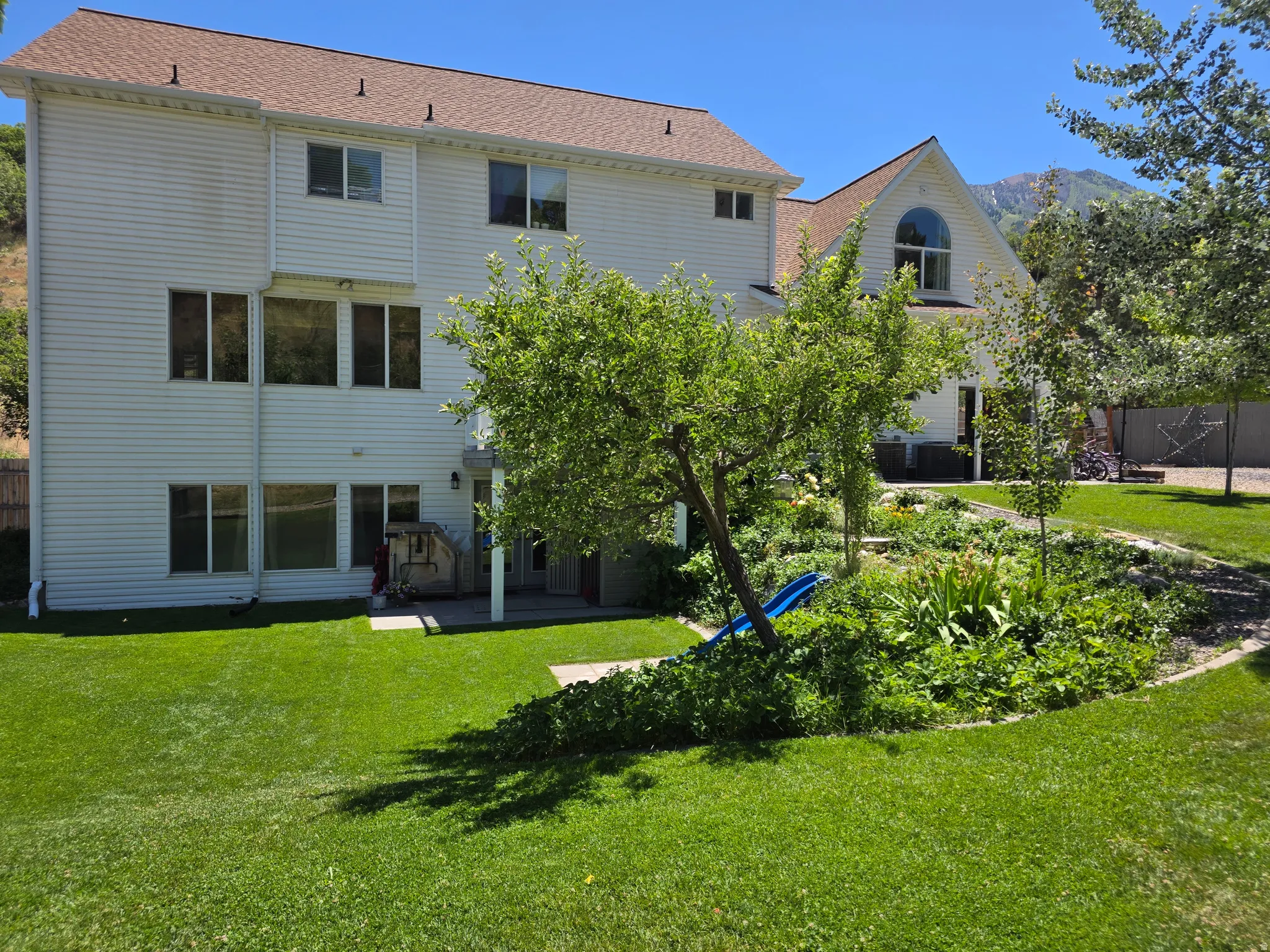 Spacious backyard featuring a lush lawn, mature trees, and tiered landscaping