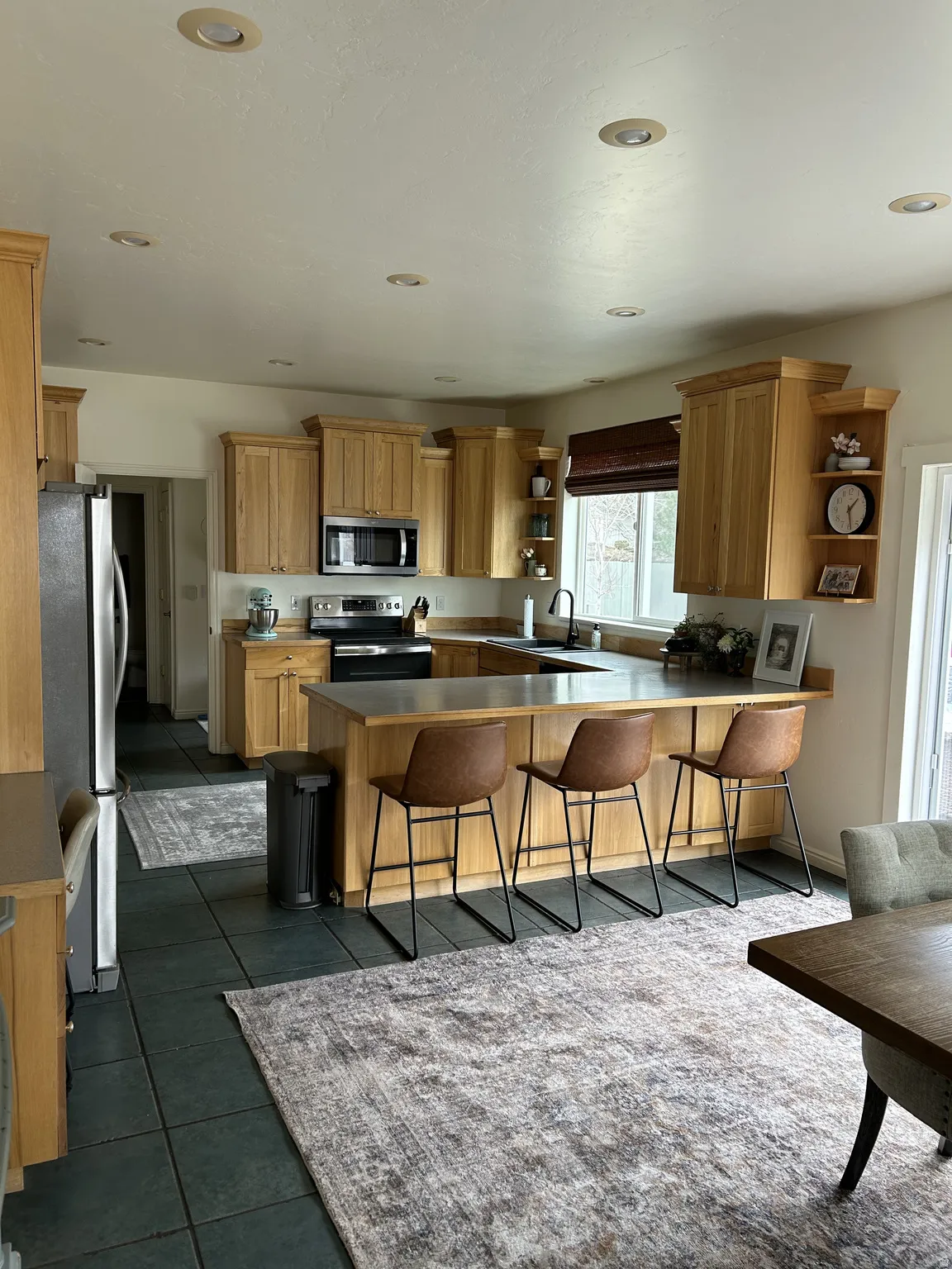 Open-concept kitchen featuring oak cabinetry, dark tile flooring, a large island with seating, recessed lighting, and stainless steel appliances