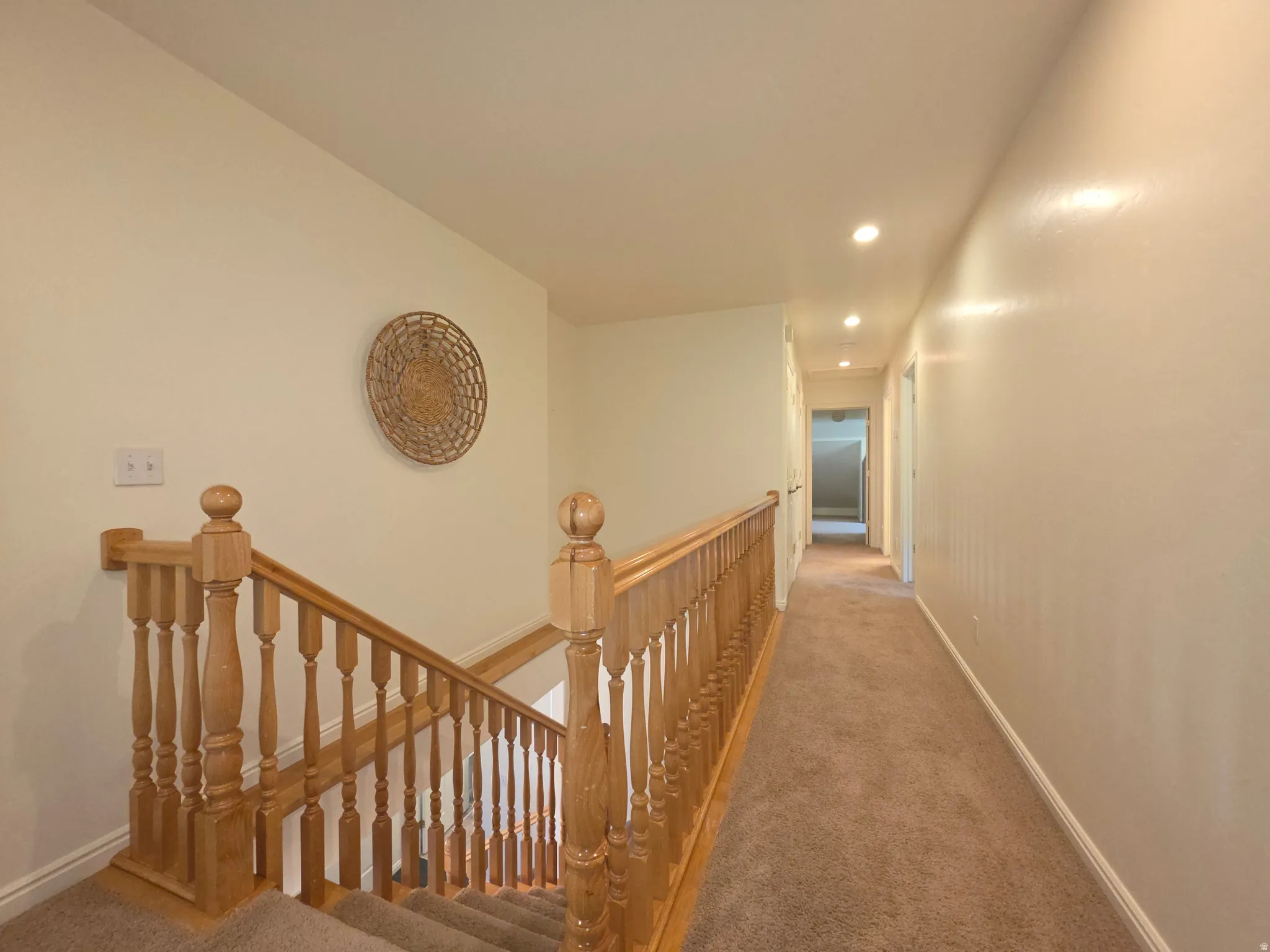 Carpeted staircase with natural wood balusters and handrail, leading to an upper-level hallway with recessed lighting and neutral wall tones