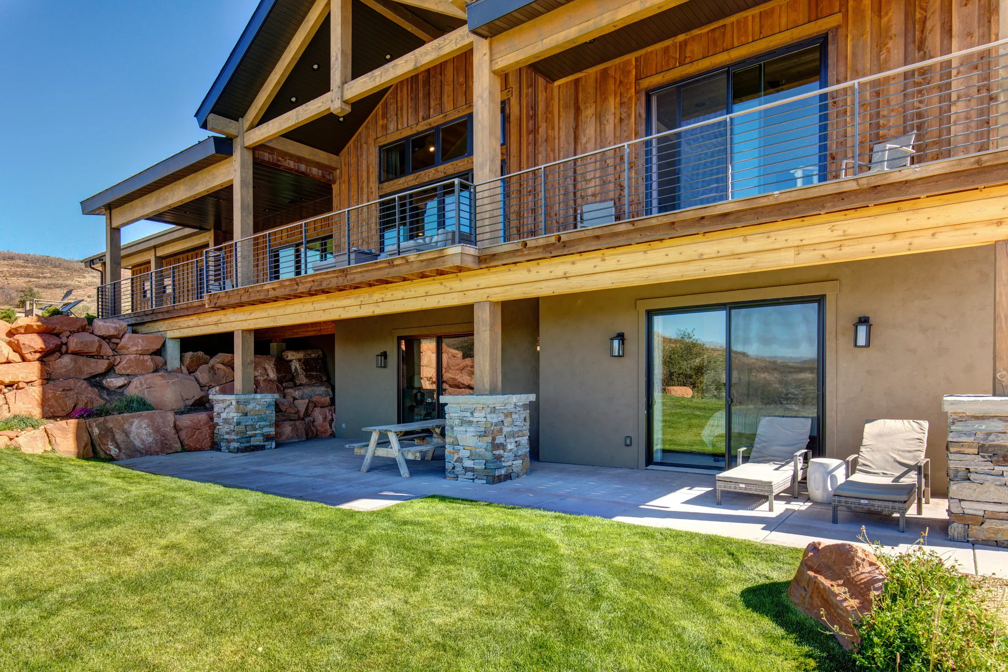 Exterior featuring a wood-finish siding upper level, ground-level patio, and natural rock landscaping